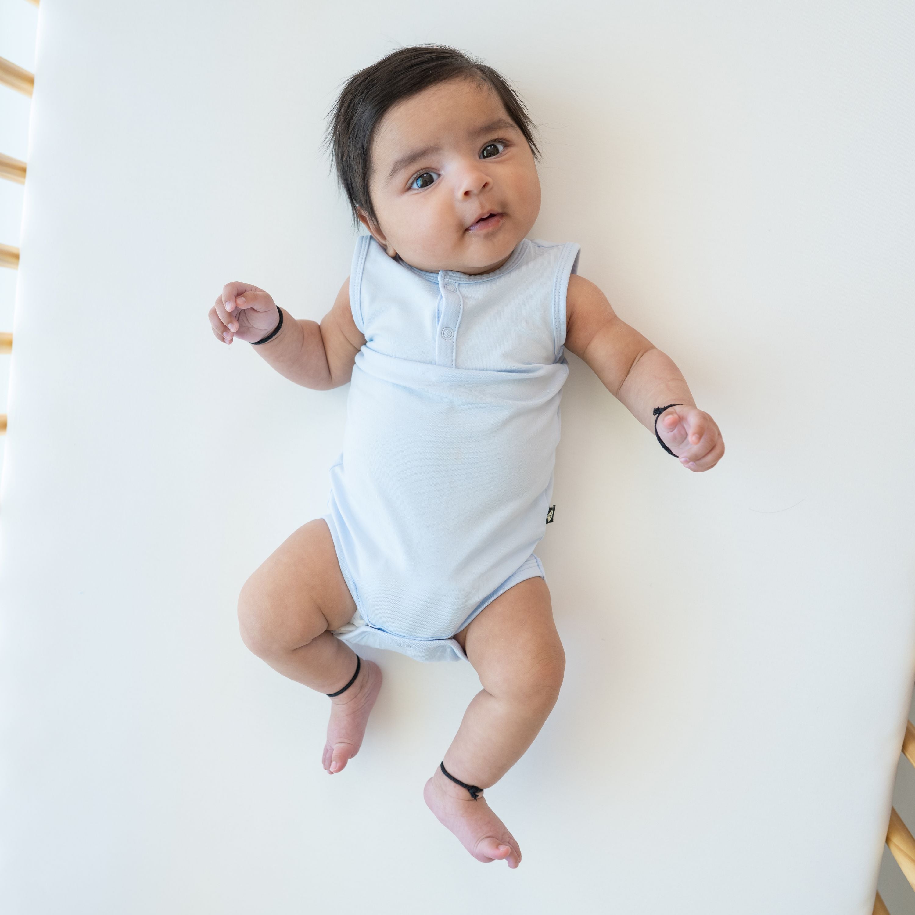 Infant model laying in a crib wearing the Sleeveless Bodysuit in Mist