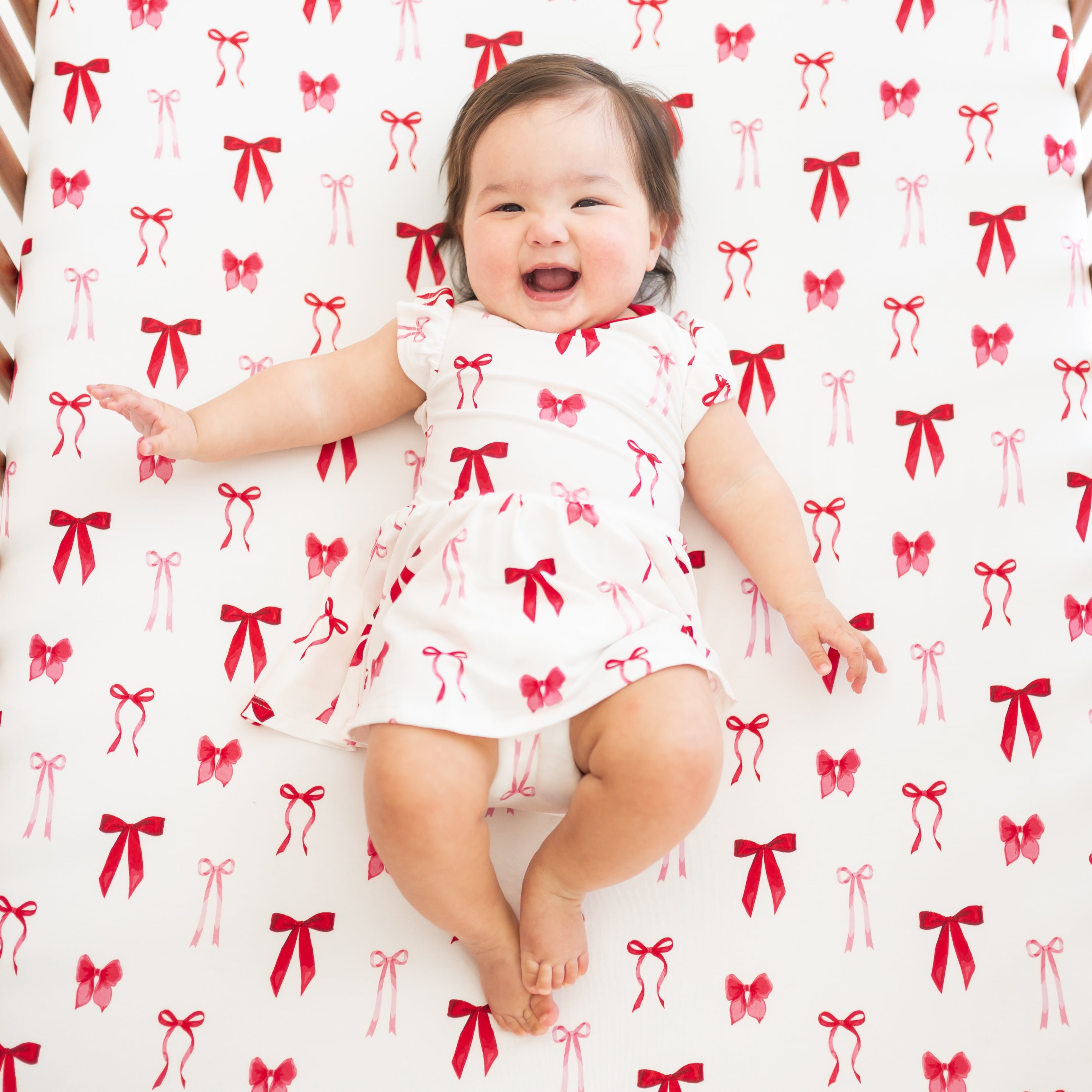 Infant laying in a crib on a Crib Sheet in Small Love Bow wearing a matching twirl bodysuit dress
