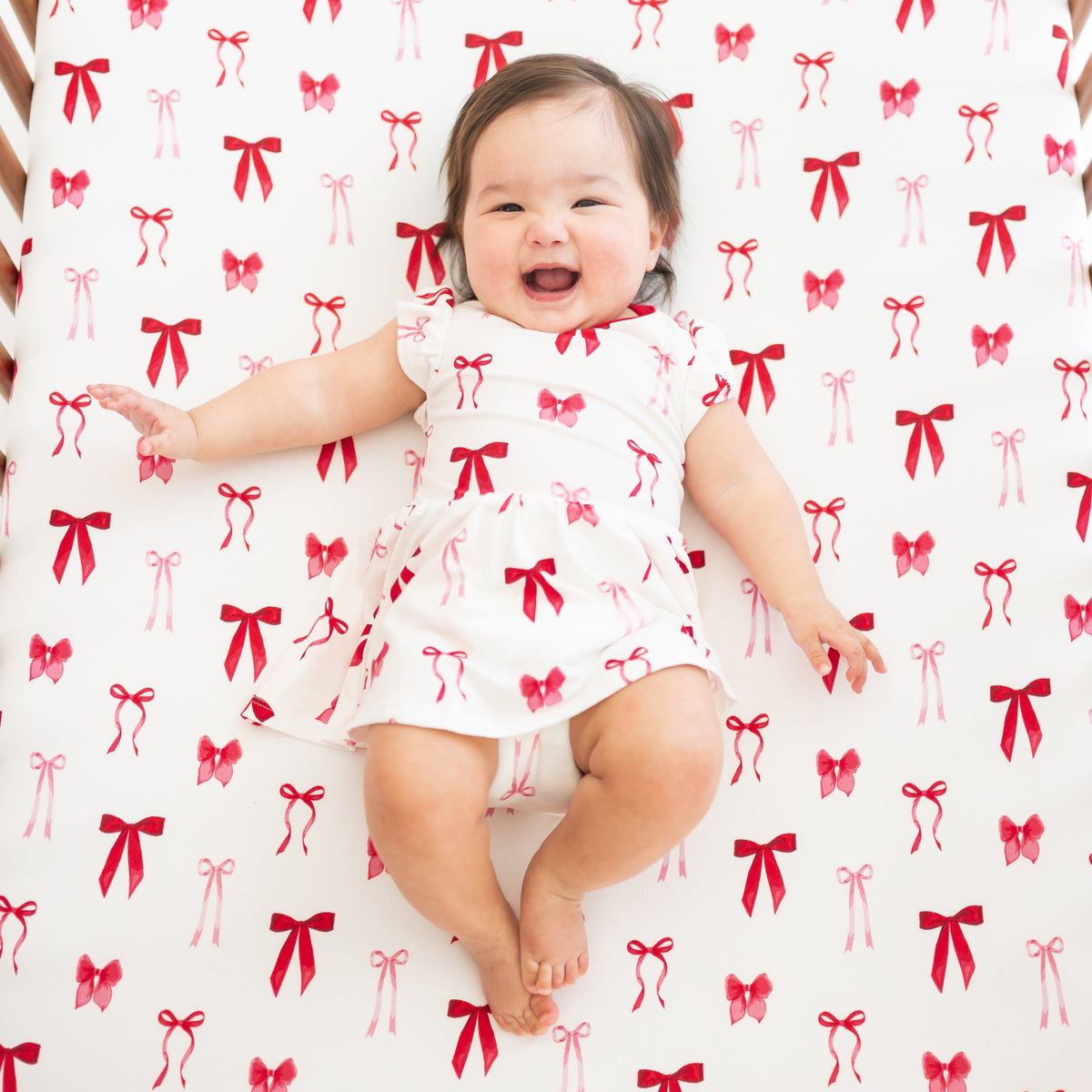 Infant laying in a crib on a Crib Sheet in Small Love Bow wearing a matching twirl bodysuit dress