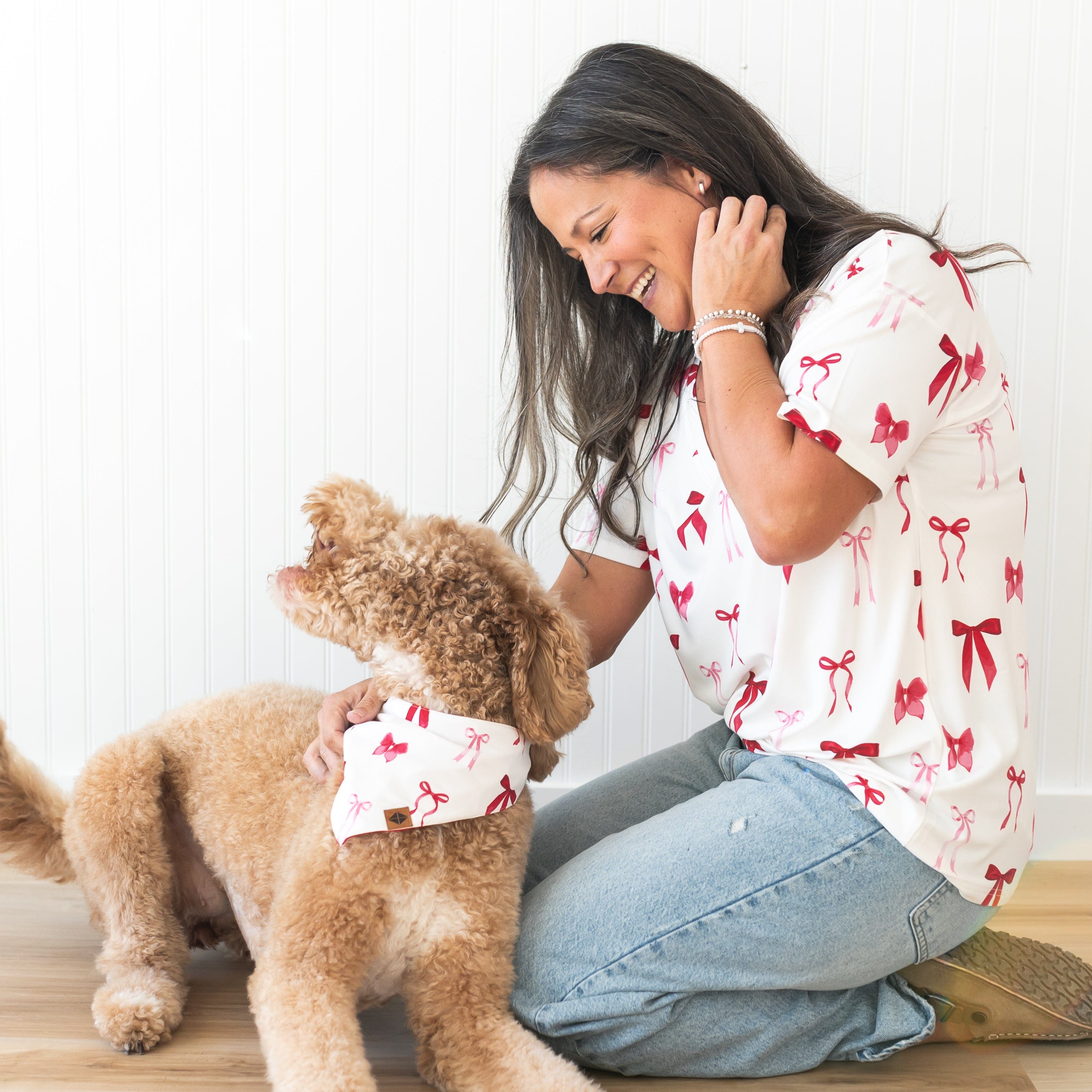 Medium sized dog laying on the floor wearing the Dog Bandana in Small Love Bow sitting beside a female wearing the Women's V-Neck in Big Love Bow