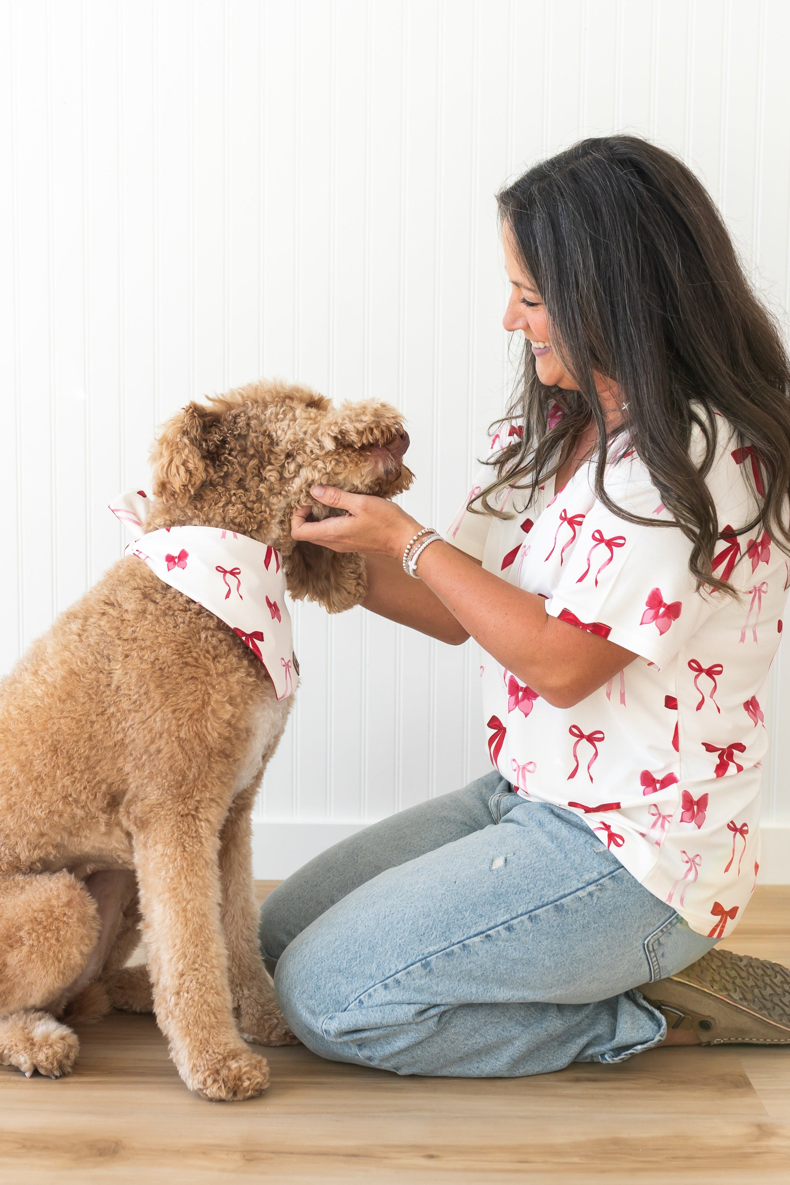 Female model wearing the Women's Relaxed Fit V-Neck in Big Love Bow sitting on the floor beside her dog who is wearing the dog bandana in small love bow