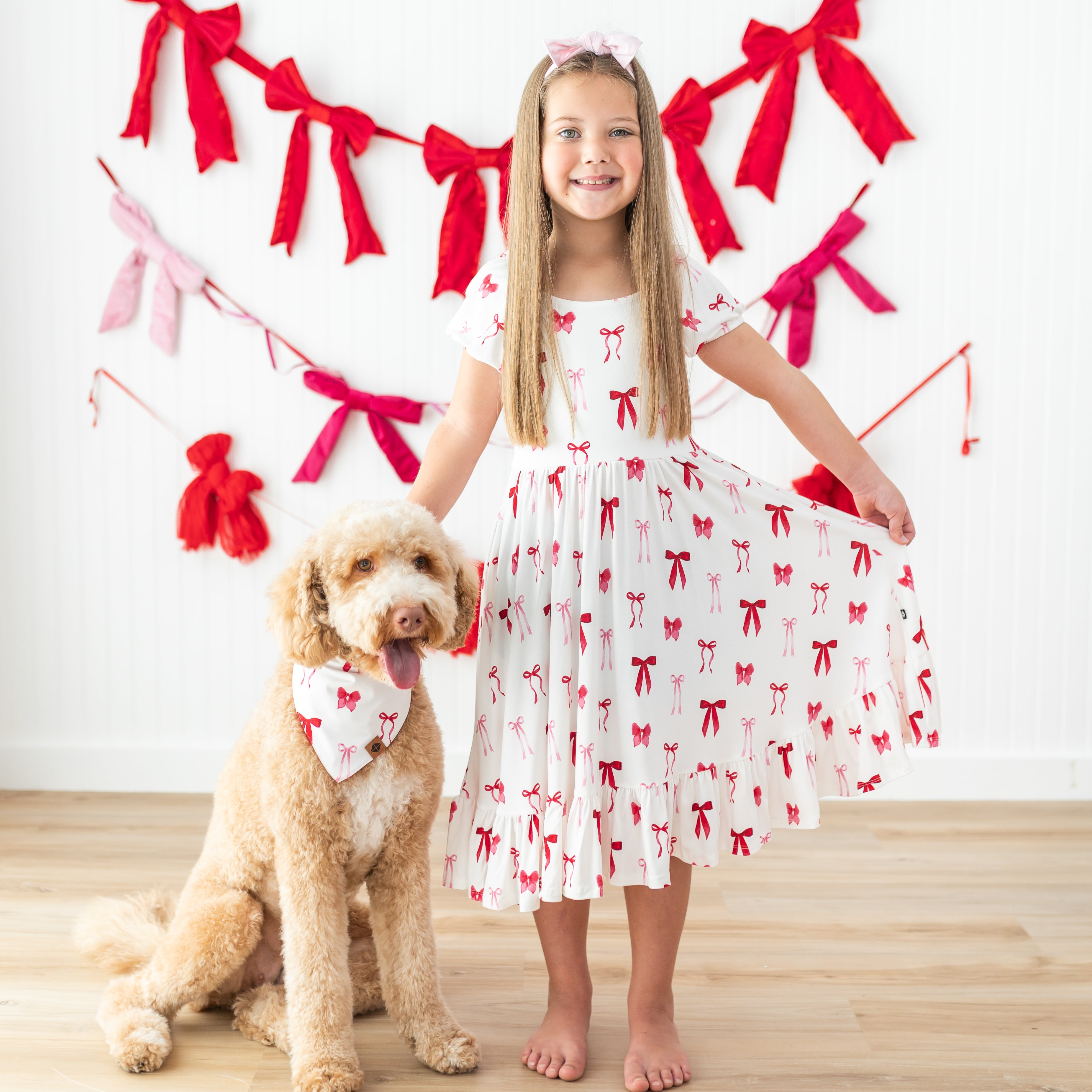 Medium sized dog wearing the Dog Bandana in Small Love Bow standing beside a young girl wearing the matching puff sleeve twirl dress