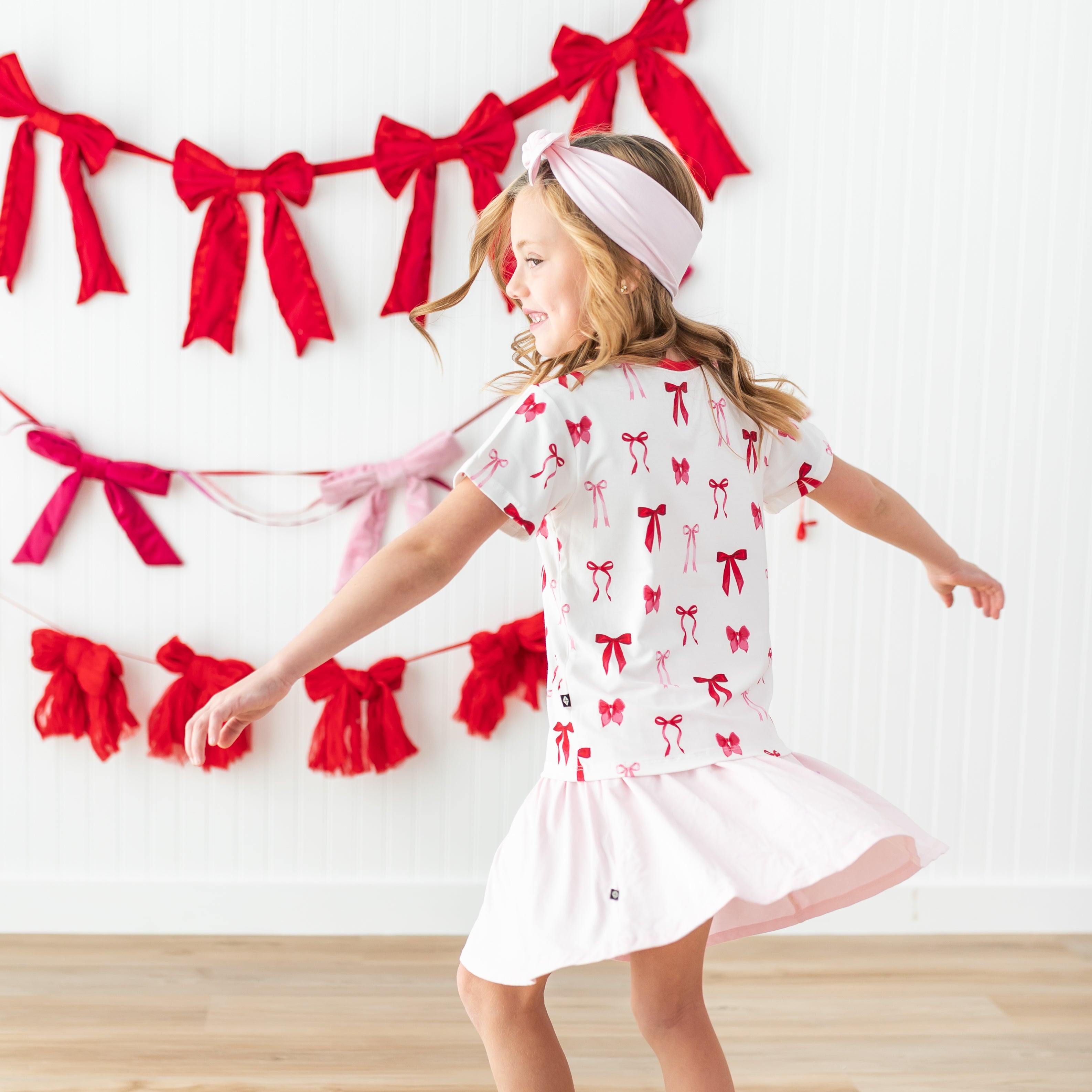 Young girl twirling wearing the Toddler V-Neck Tee in Small Love Bow paired with a sakura skort and sakura bow headband