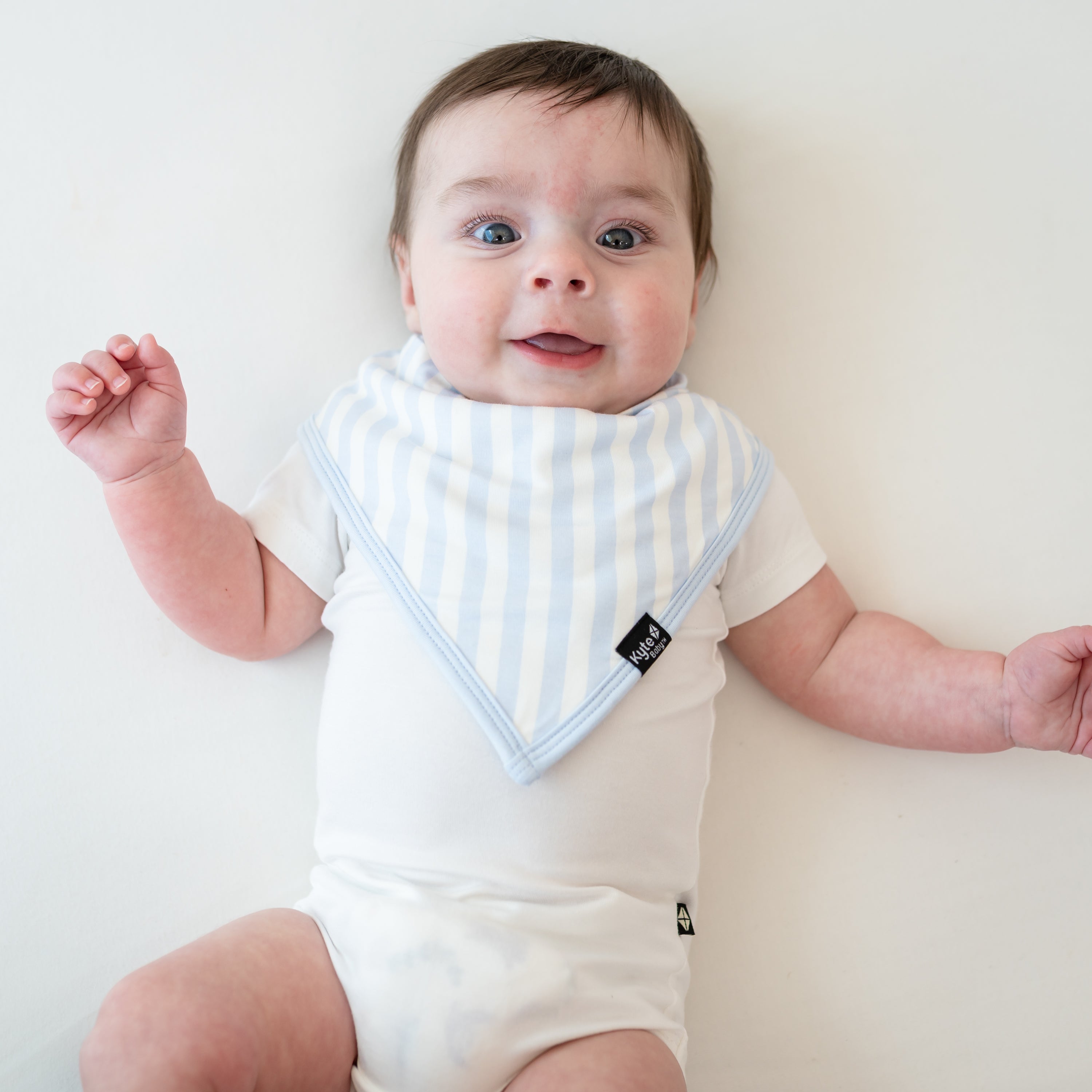 Smiling infant wearing the Bib in Big Mist Stripe paired with a Cloud Short Sleeve Bodysuit