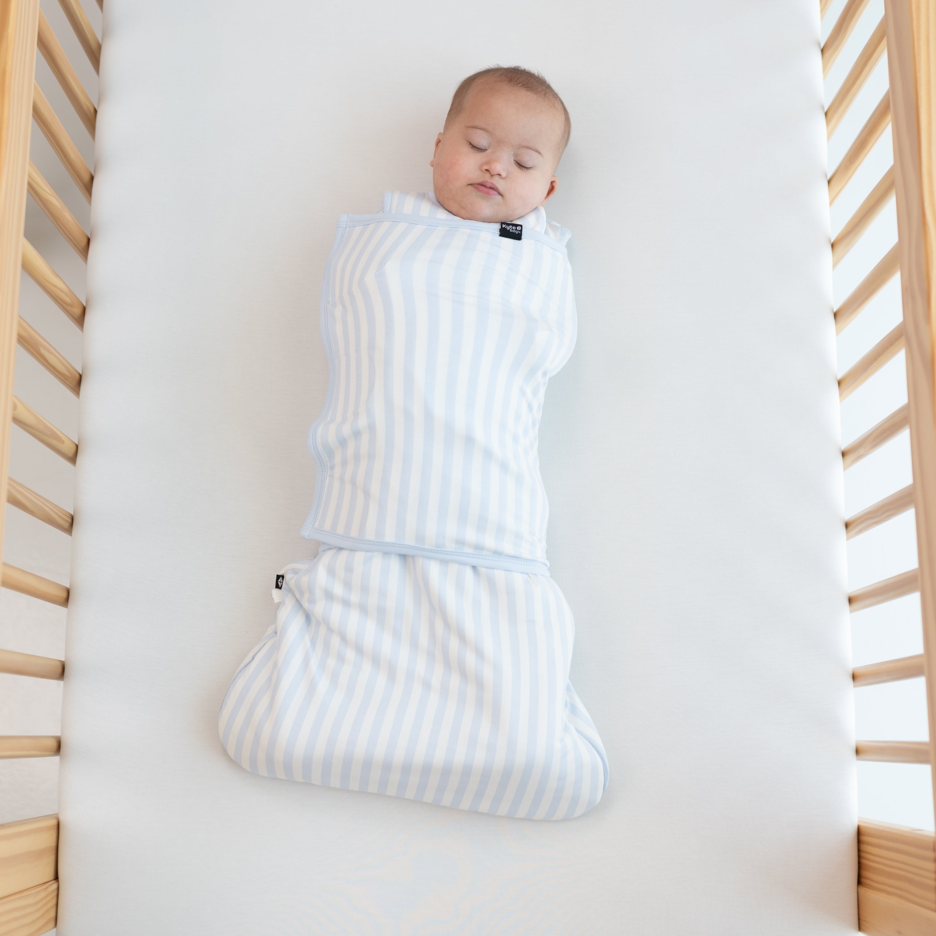 Sleeping Baby laying in a crib swaddled in the Sleep Bag Swaddler in Small Mist Stripe 1.0