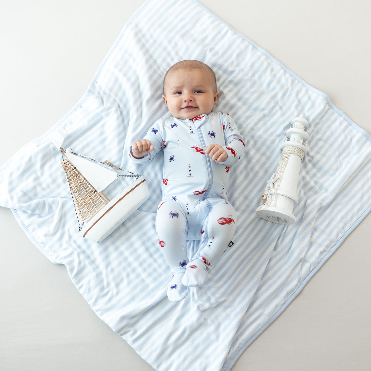 Infant laying on a Baby Blanket in Small Mist Stripe TOG 1.0 wearing Harbor Zippered Footie pajamas