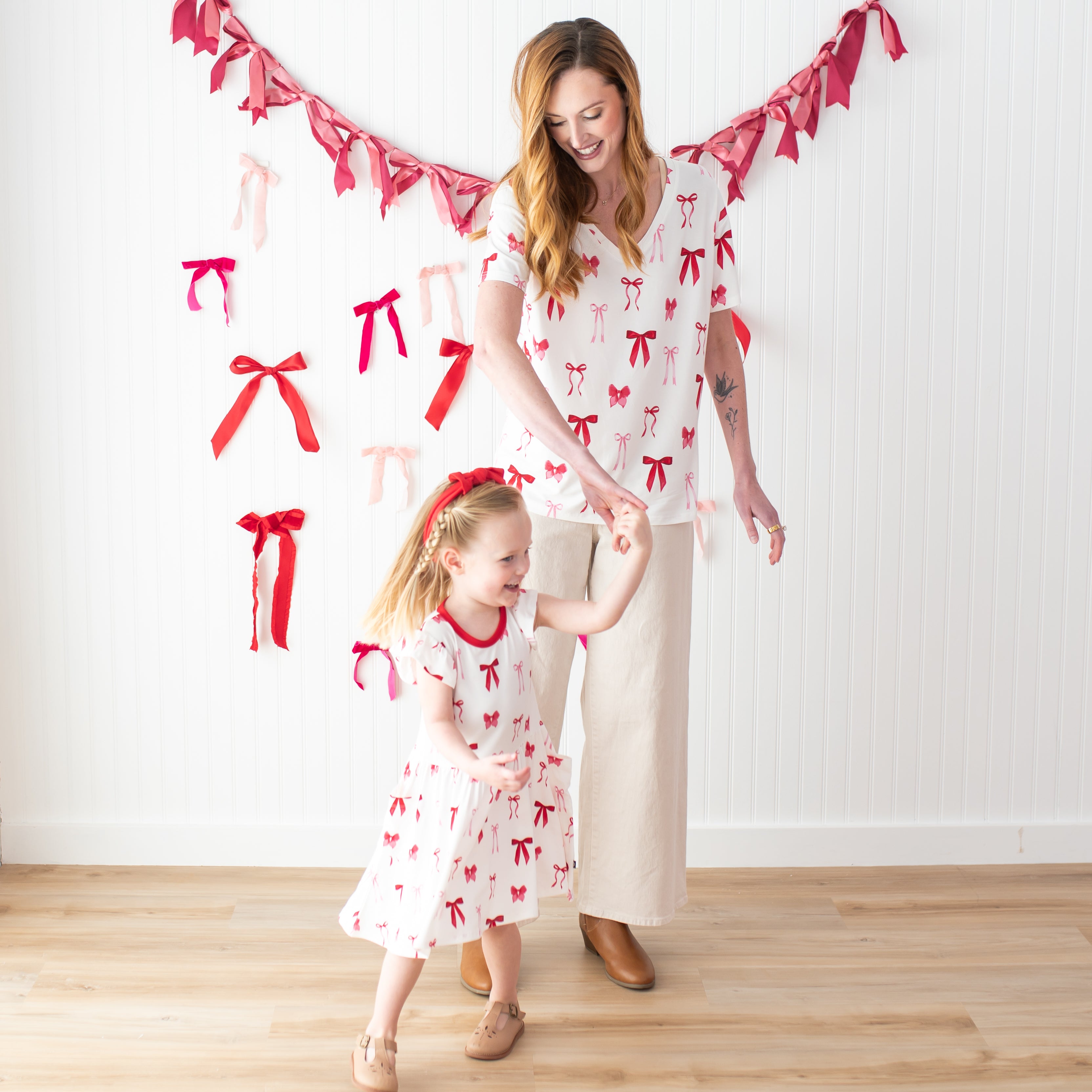 Young girl wearing the Pocket Dress in Small Love Bow being twirled by her mother wearing the Women's V-Neck in Big Love Bow