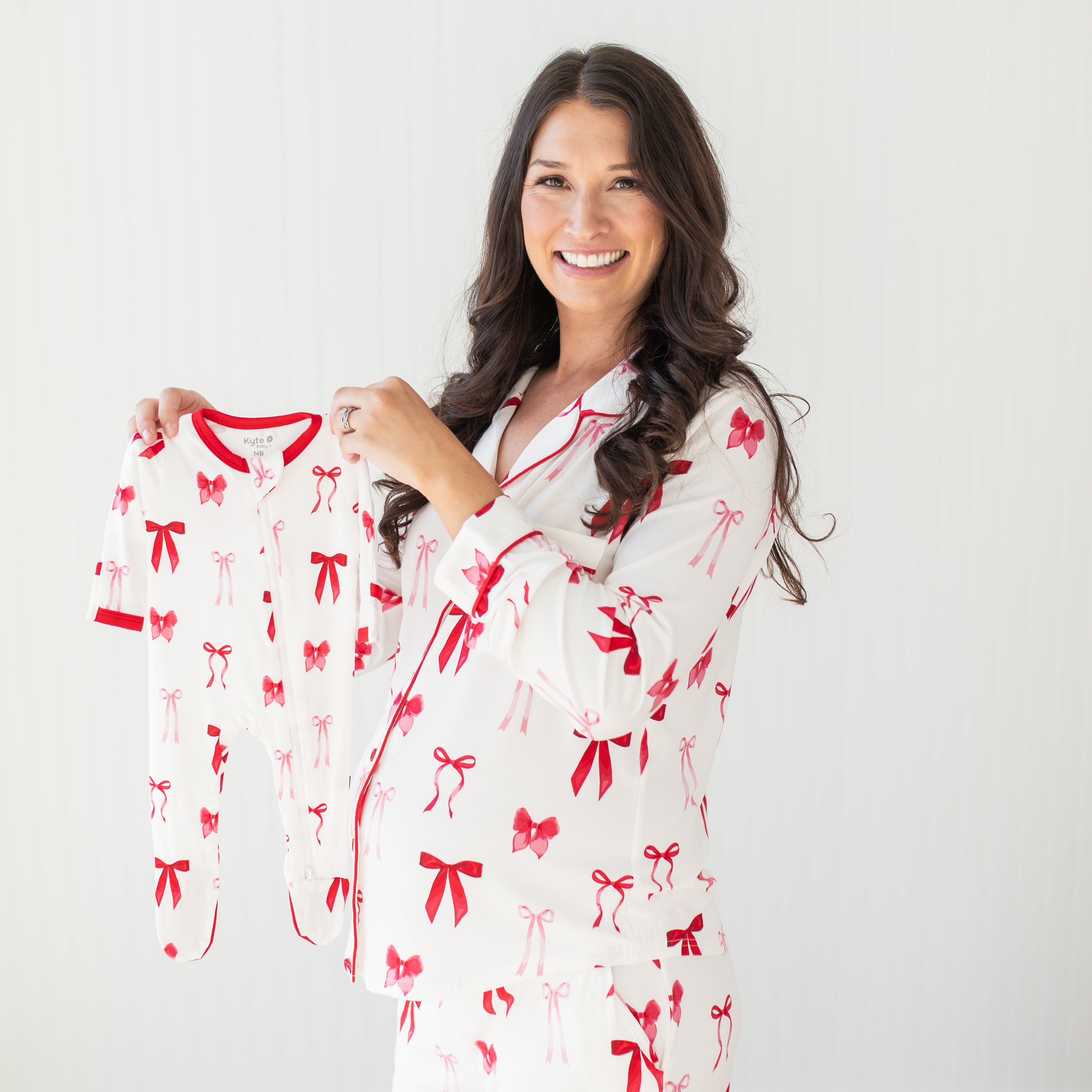 Expectant mother wearing the women's long sleeve pajama set in Big Love bow holding a Zippered Footie in Small Love Bow