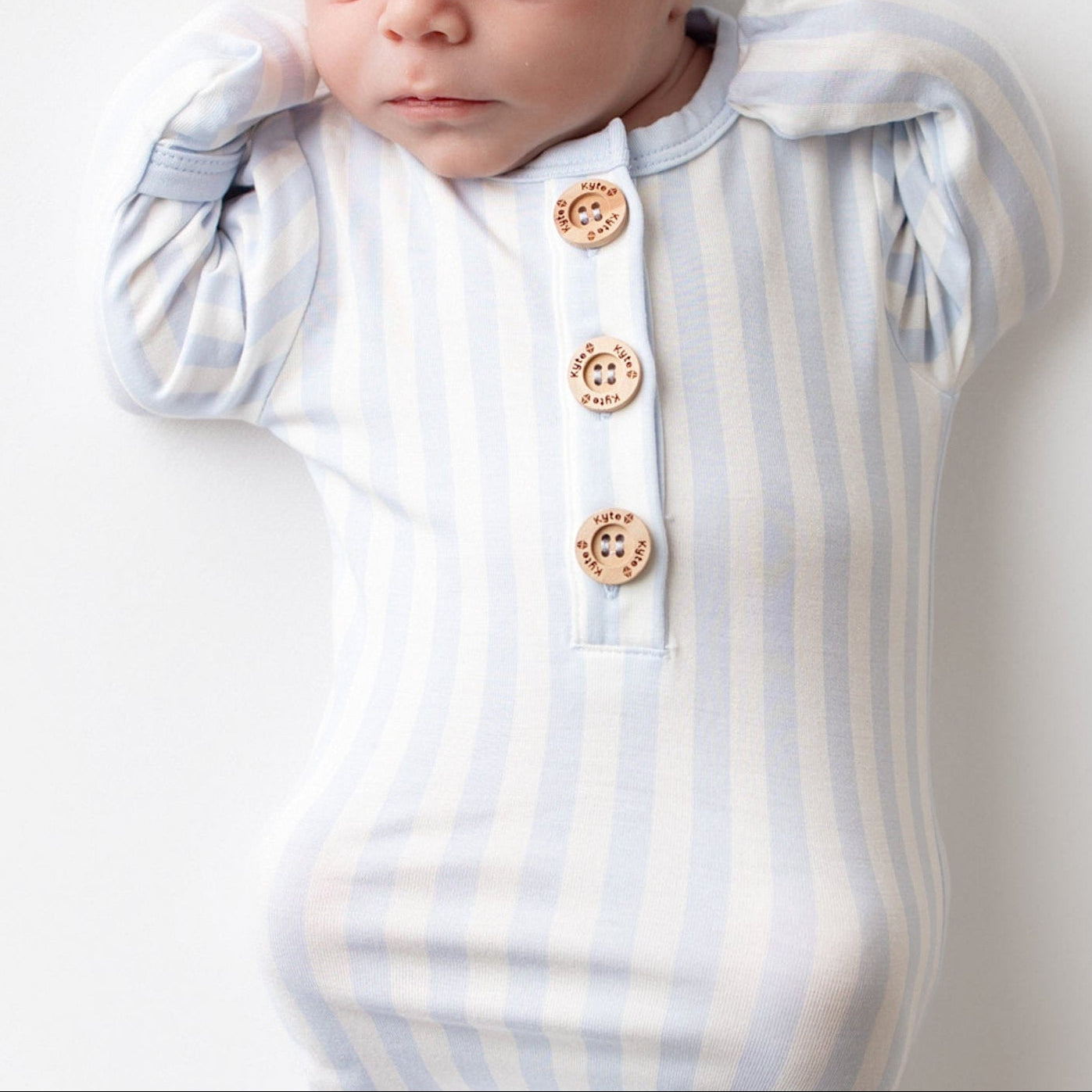 newborn laying down on a light neutral surface wearing the Knotted Gown with Hat Set in Small Mist Stripe