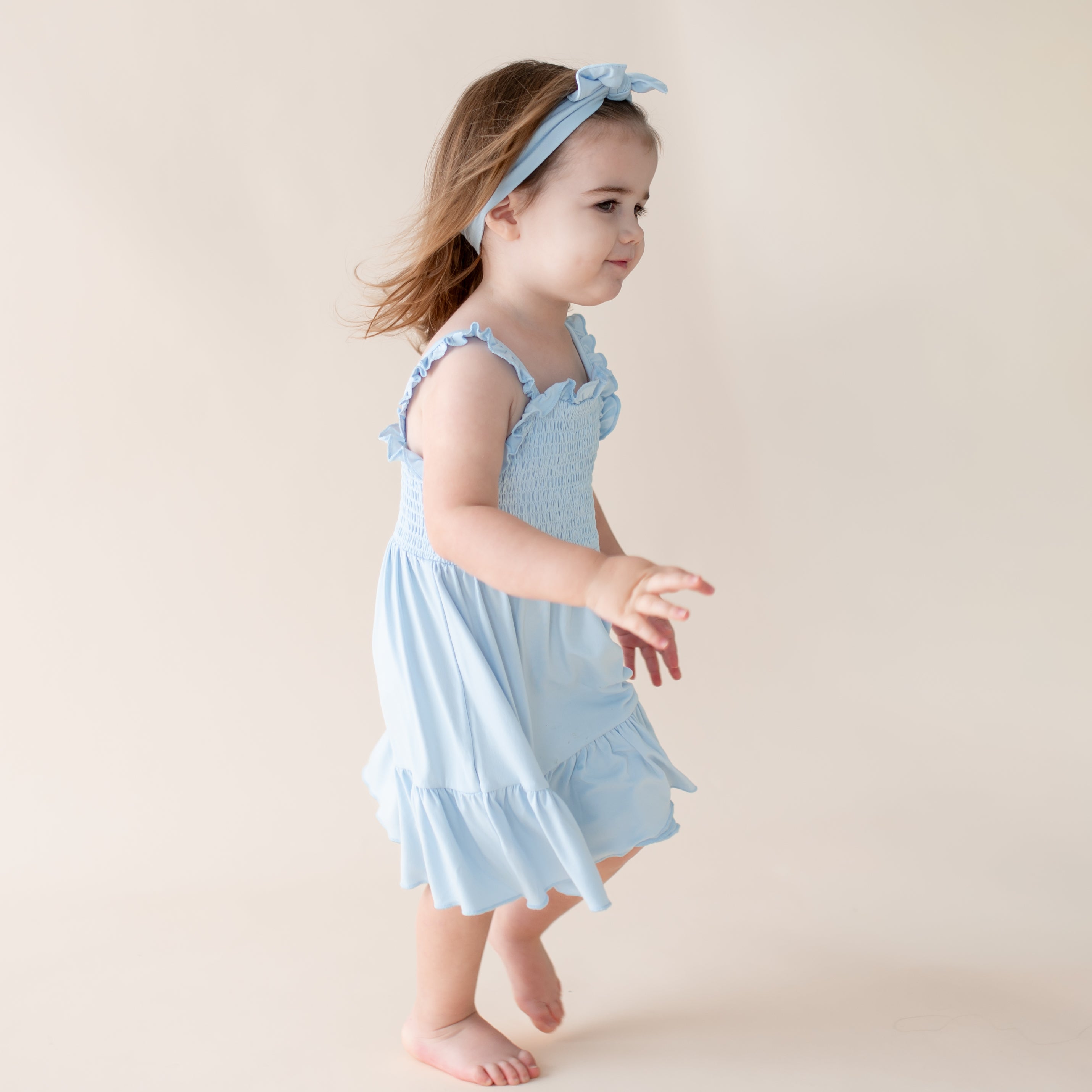Young girl wearing a ruffle sleeve smocked dress and matching bow