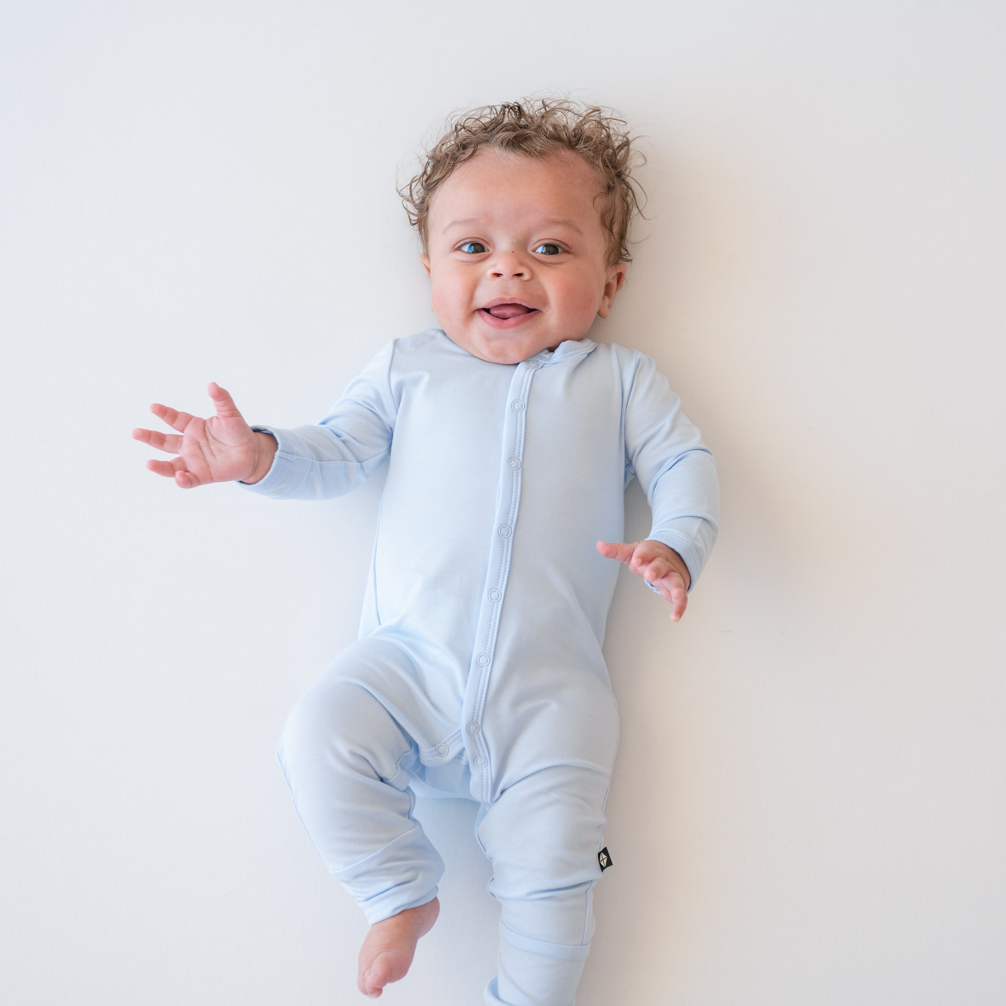 Smiling infant model laying down wearing the Romper in Mist