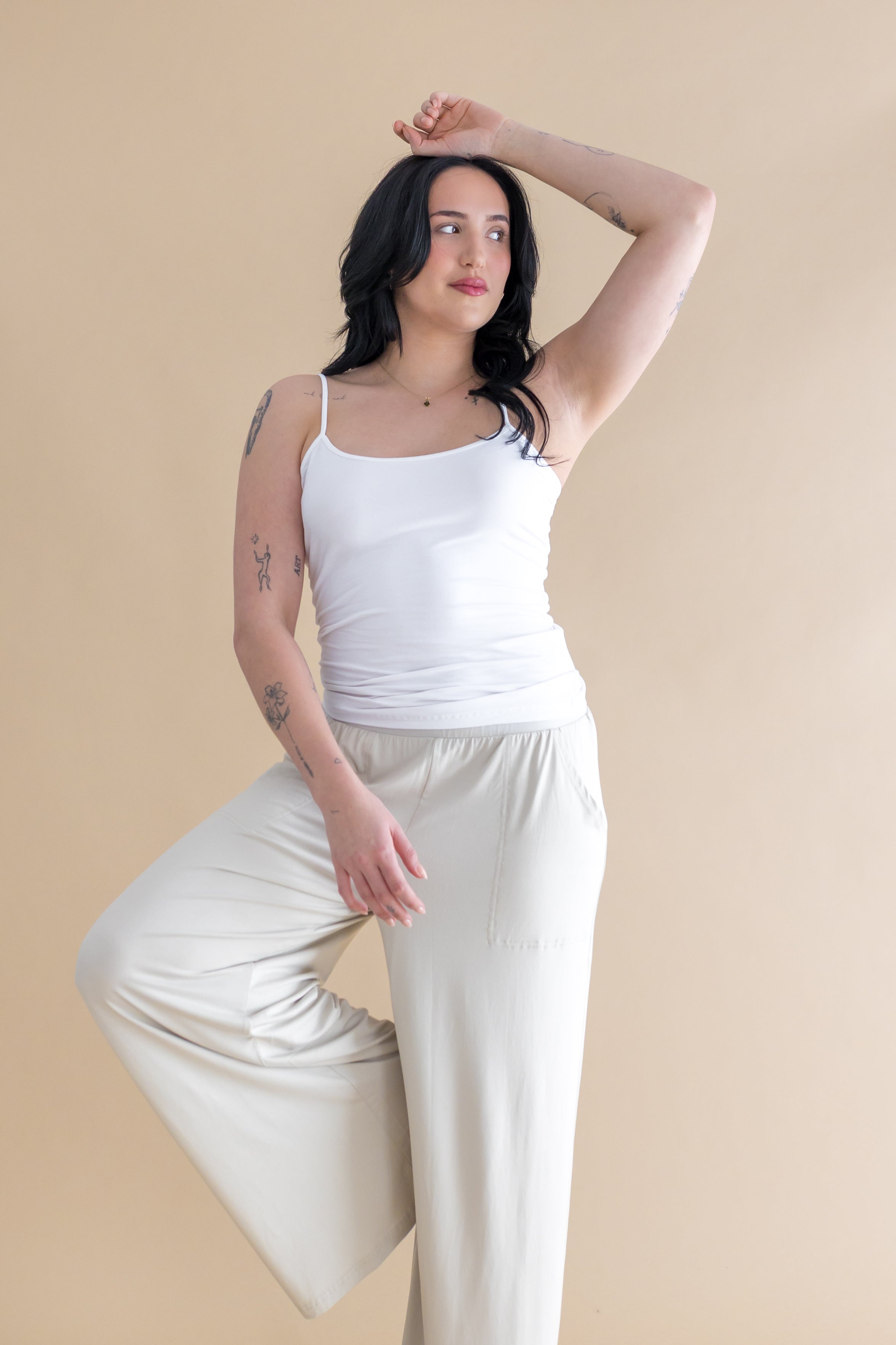 Woman wearing a white tank top and beige pants against a beige background