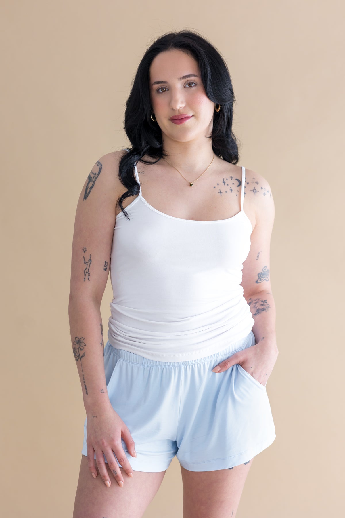 Woman wearing a white tank top and light blue shorts against a beige background