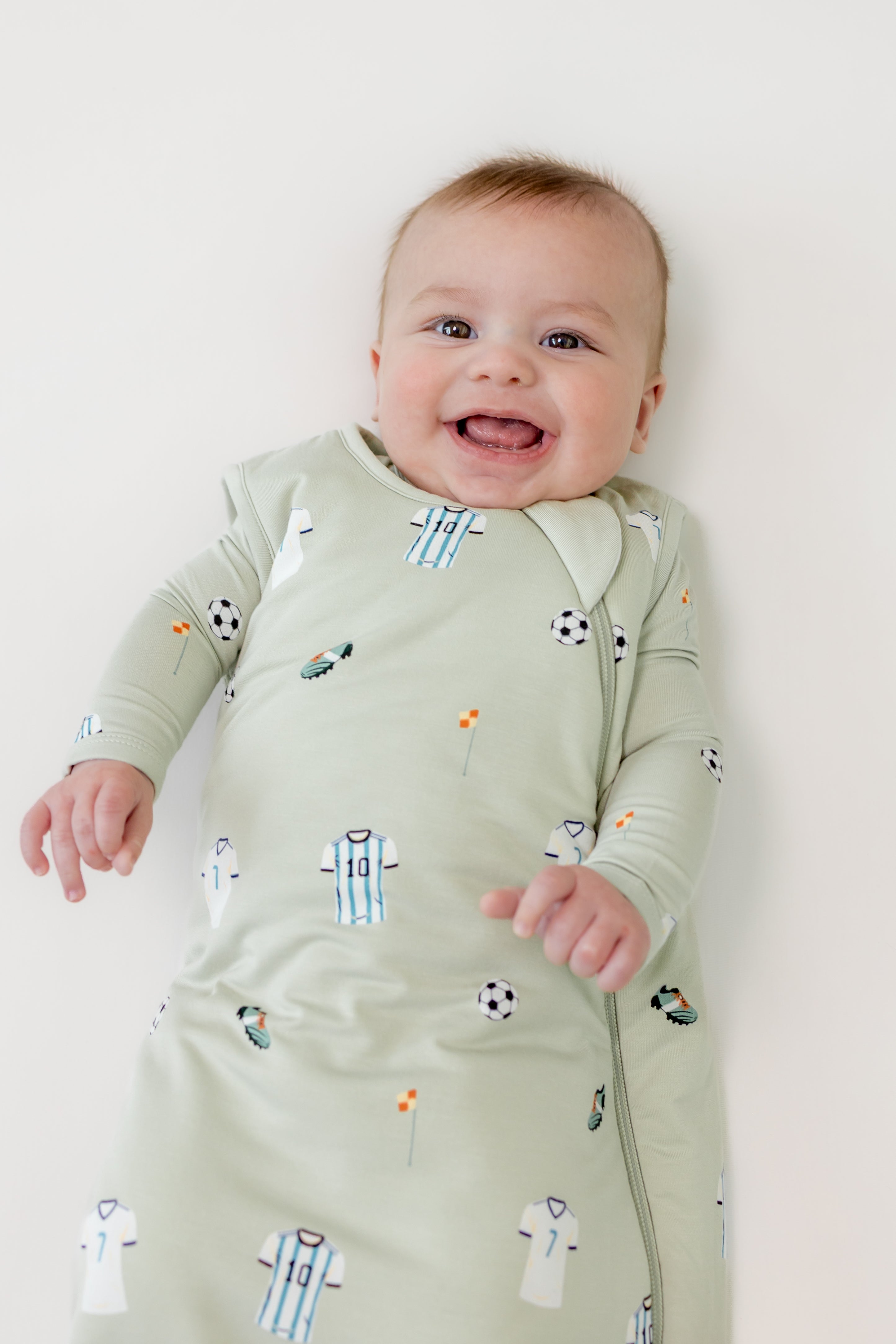 Baby smiling in Soccer print sleep bag on a beige background