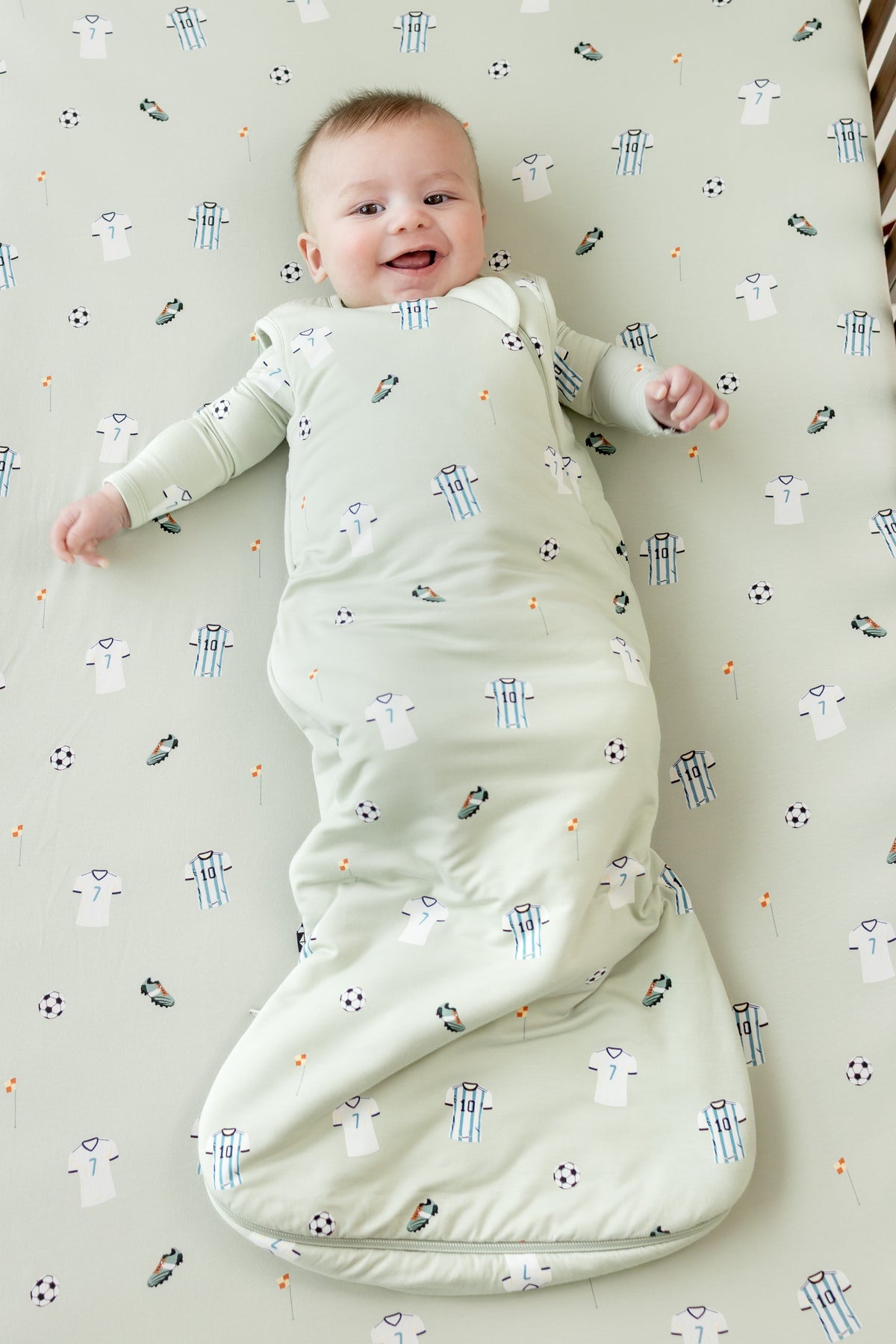 Baby lying on a Soccer print Crib sheet wearing Soccer print sleep bag