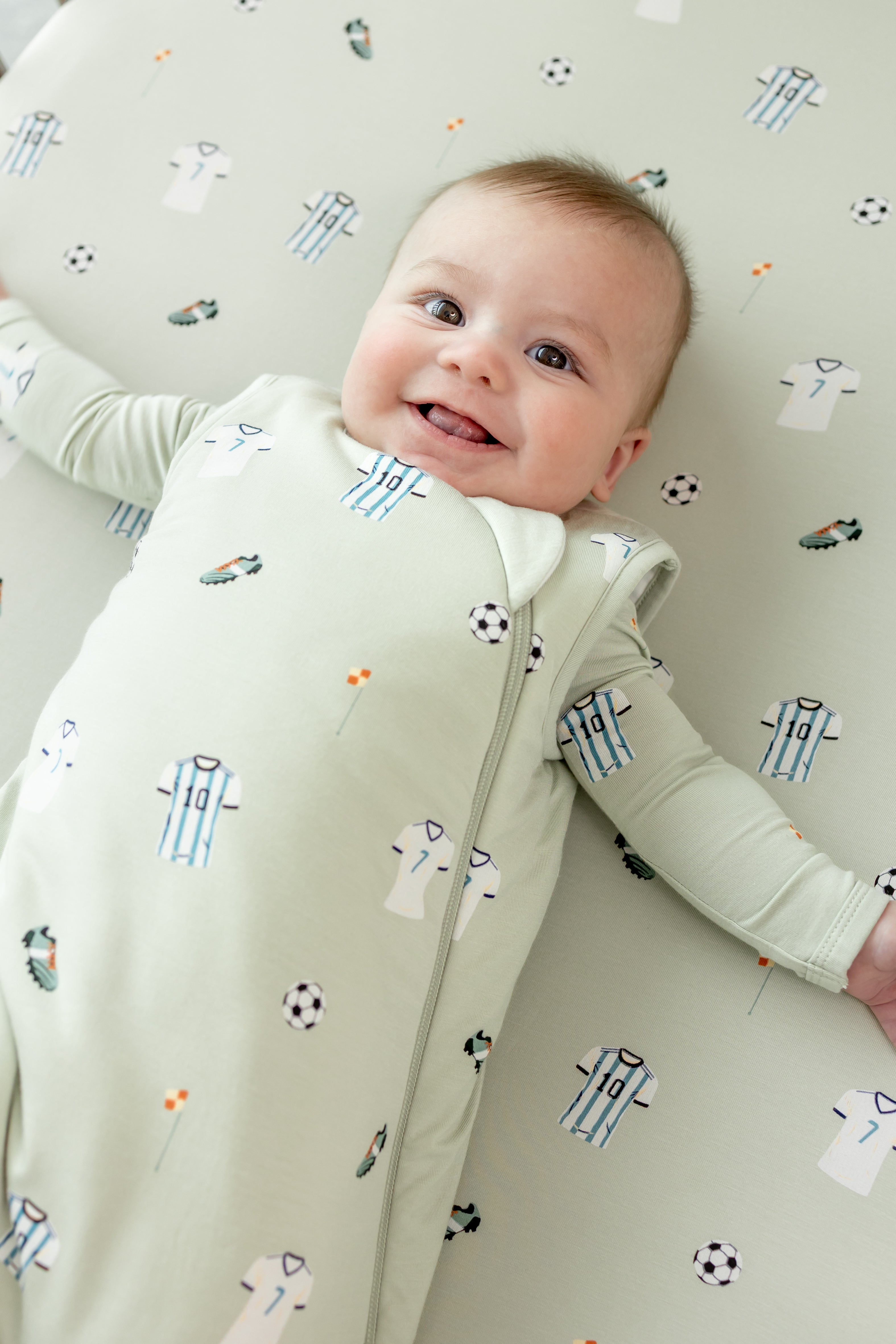Baby smiling on Soccer print Crib sheet in a soccer print sleep bag