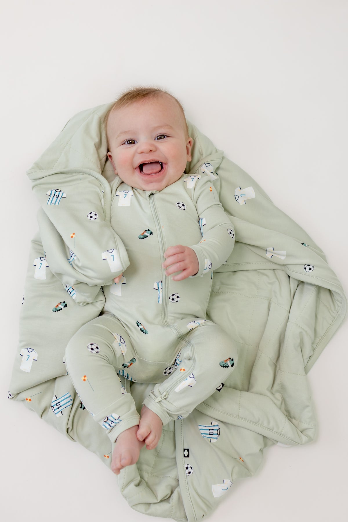 Baby wrapped in Soccer print Baby Blanket wearing a soccer print zippered romper on a beige background