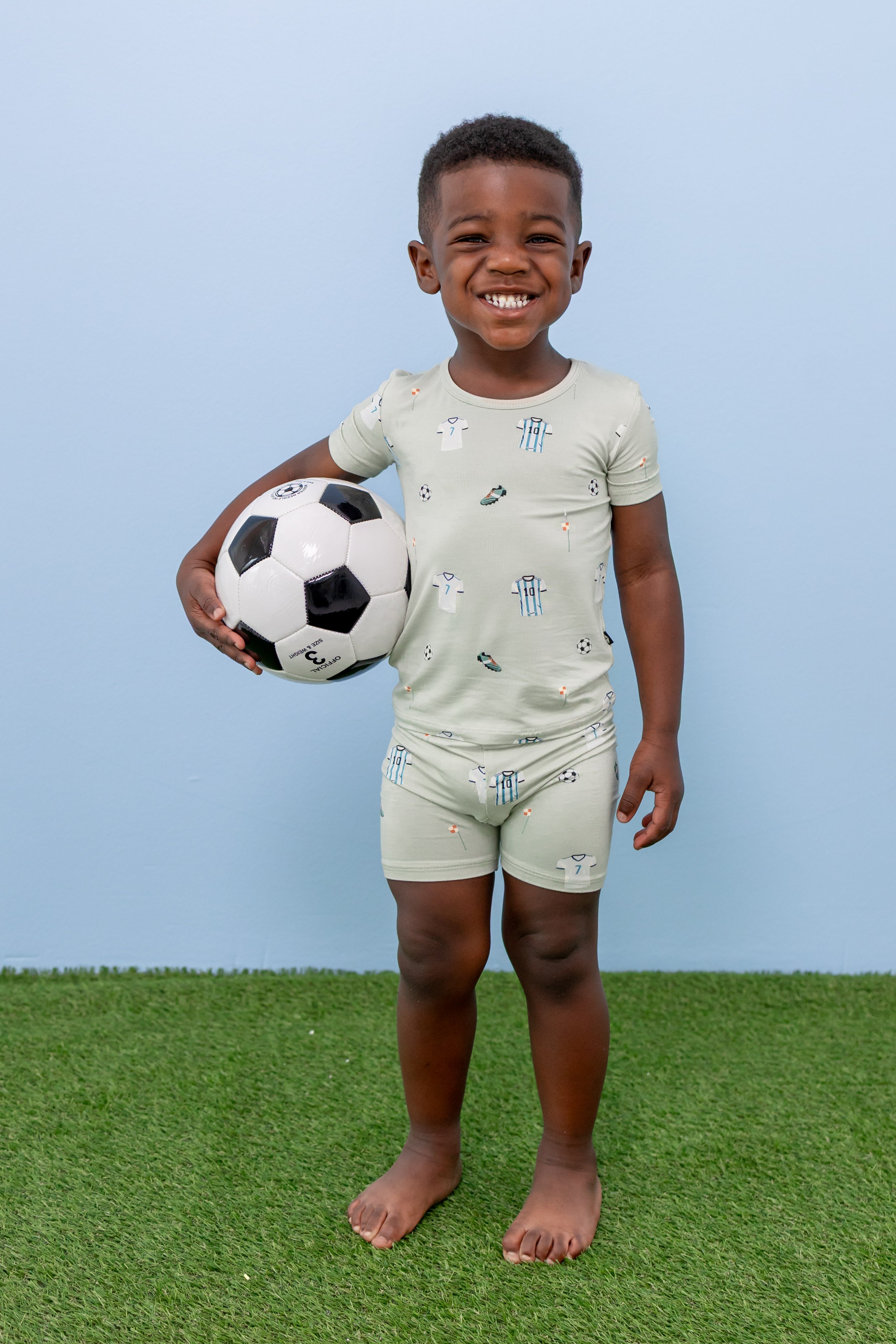 Child wearing short sleeve pajama set in Soccer print on green grass with a soccer ball