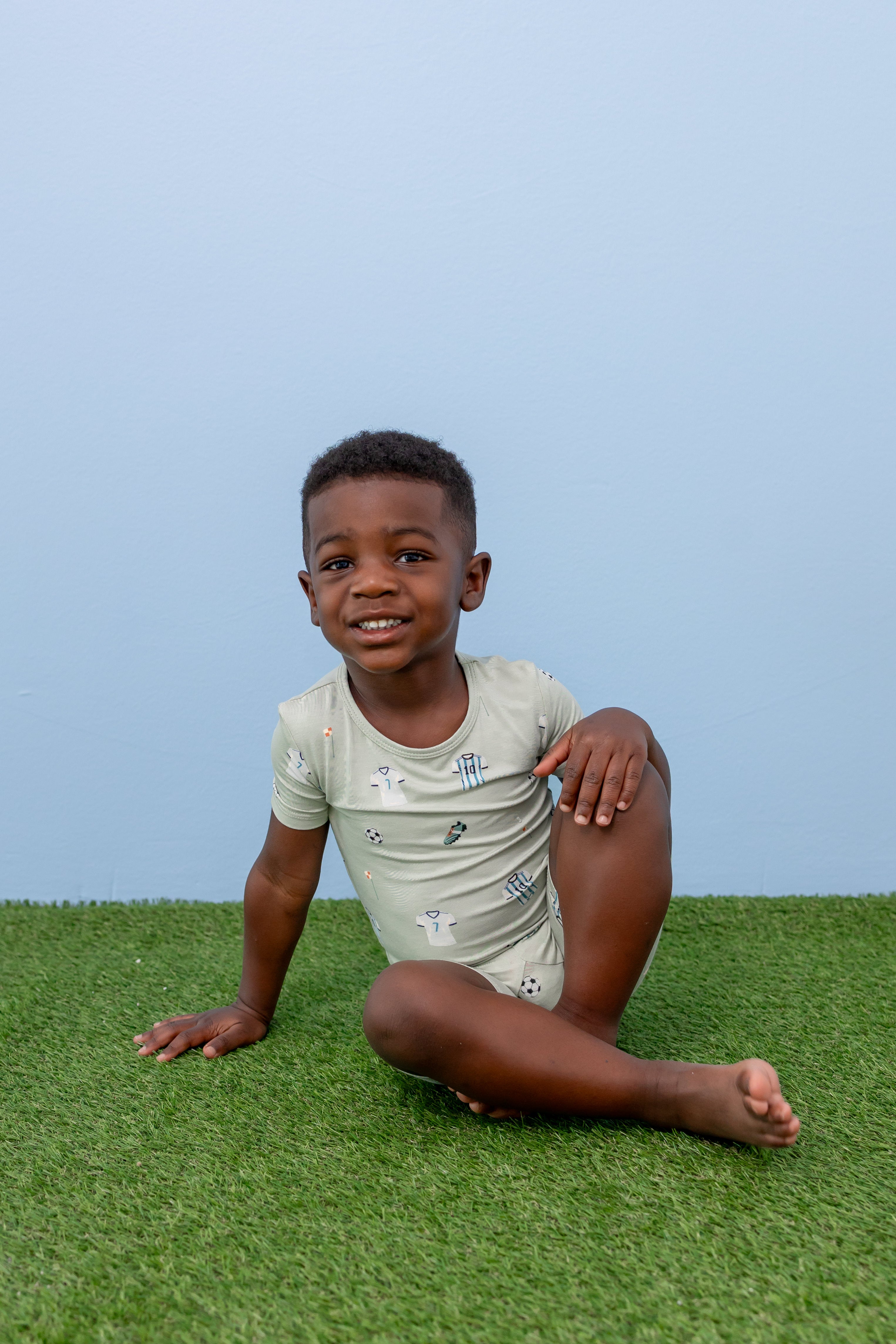 Child sitting in Soccer print short sleeve pajama set on green grass