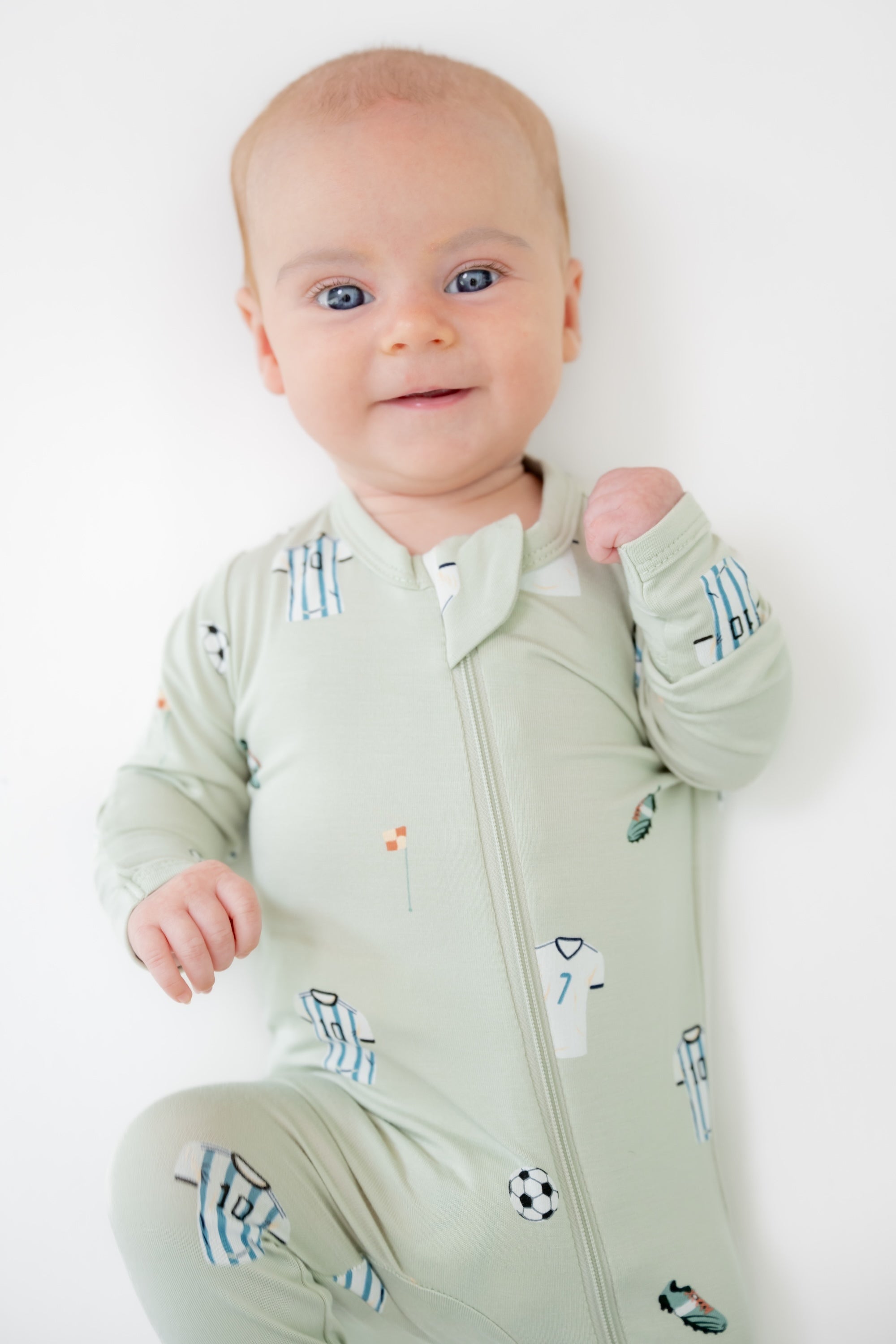 Baby wearing zippered footie in Soccer print on a white background