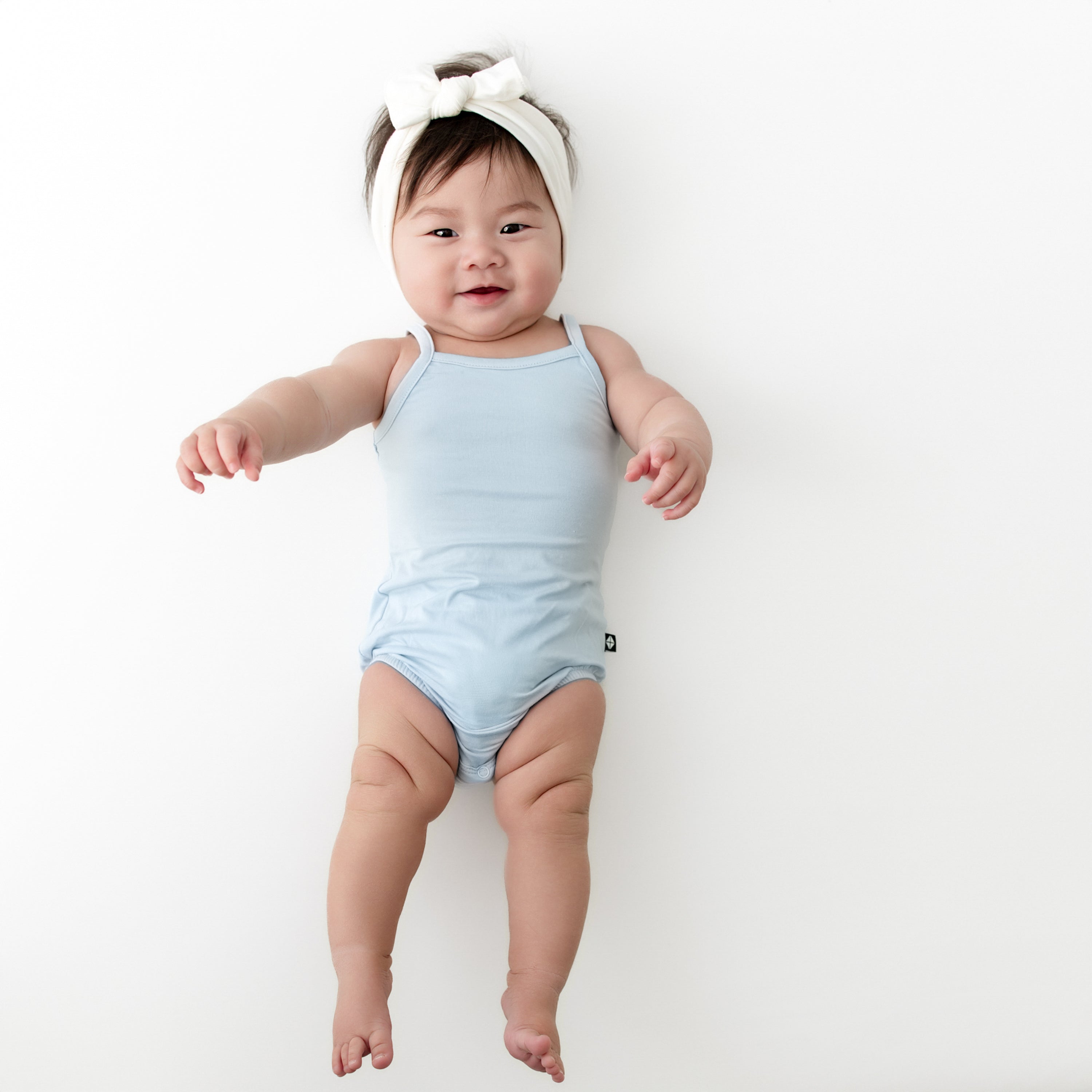 Young infant wearing the Spaghetti Strap Leotard in Breeze on a light cream surface