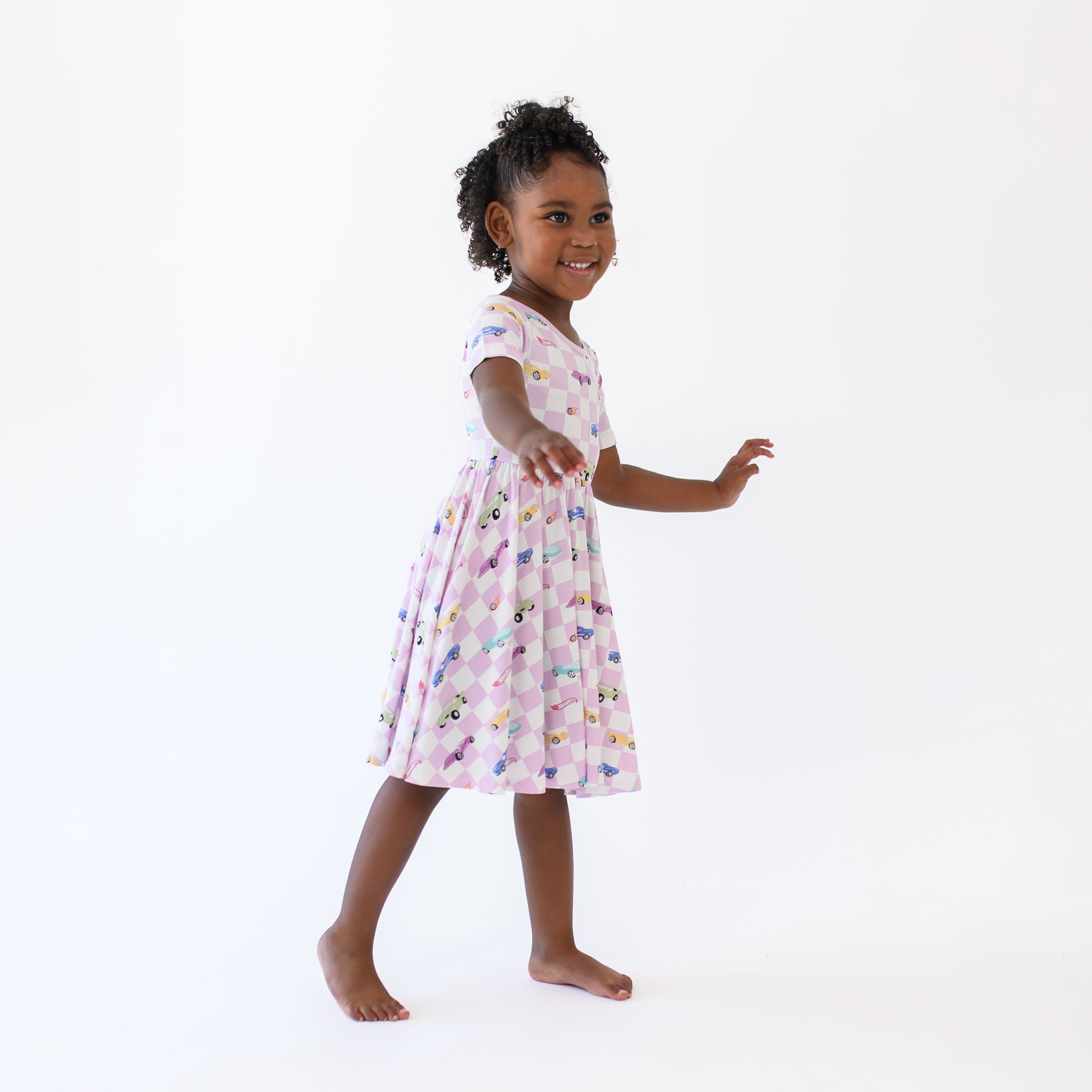 Smiling girl model standing with arms out wearing the Twirl Dress in Sparkles and Speed