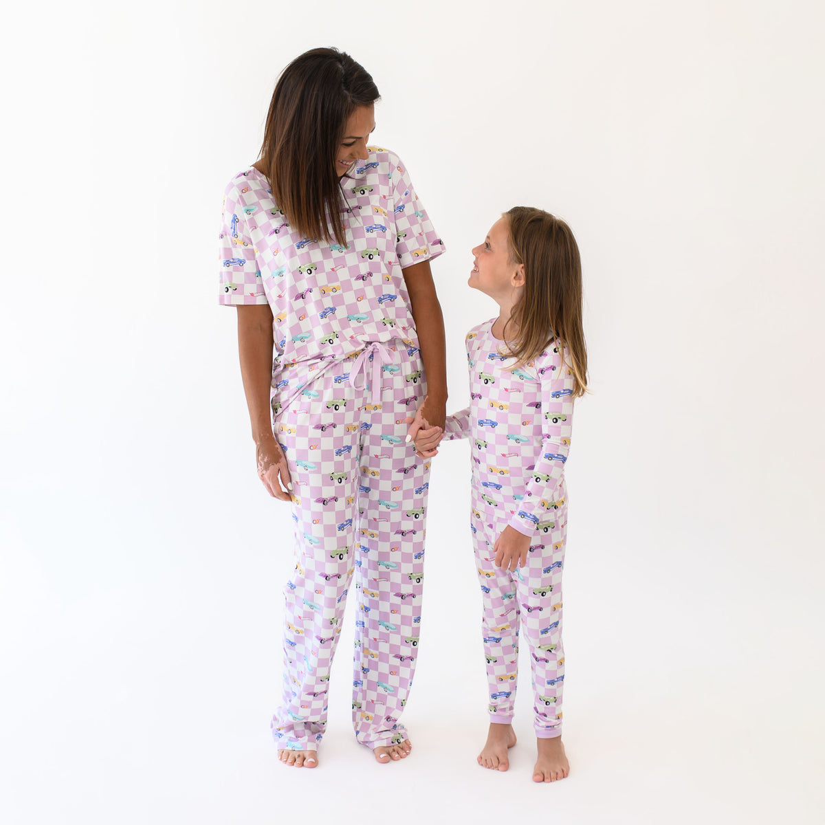 Mother and daughter holding hands looking at one another matching in Sparkles and Speed. Mother wearing the Women's Lounge Pants in Sparkles and Speed and women's relaxed vneck and child wearing the long sleeve toddler pajama set