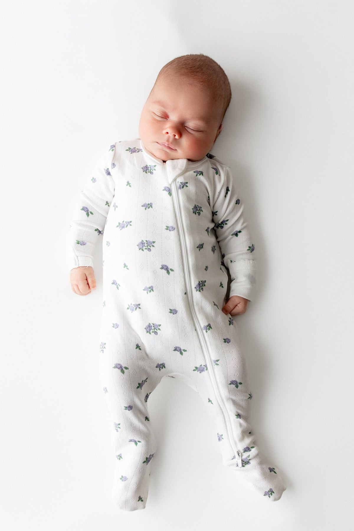 Sleeping newborn wearing the Pointelle Zippered Footie in Spray Rose