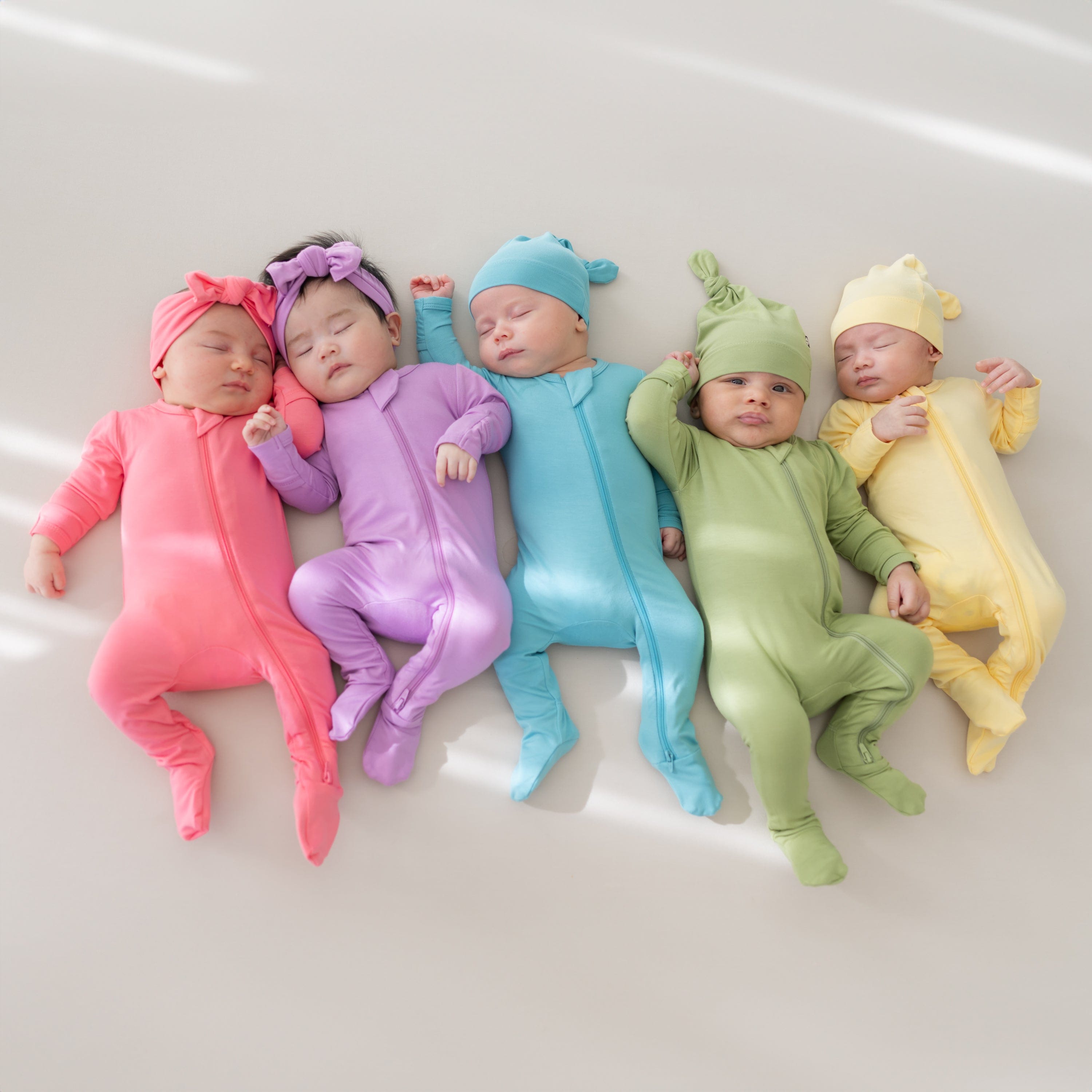 Babies in zippered footies with matching bows and knotted caps in Spring 2025 Hawaii-inspired solids