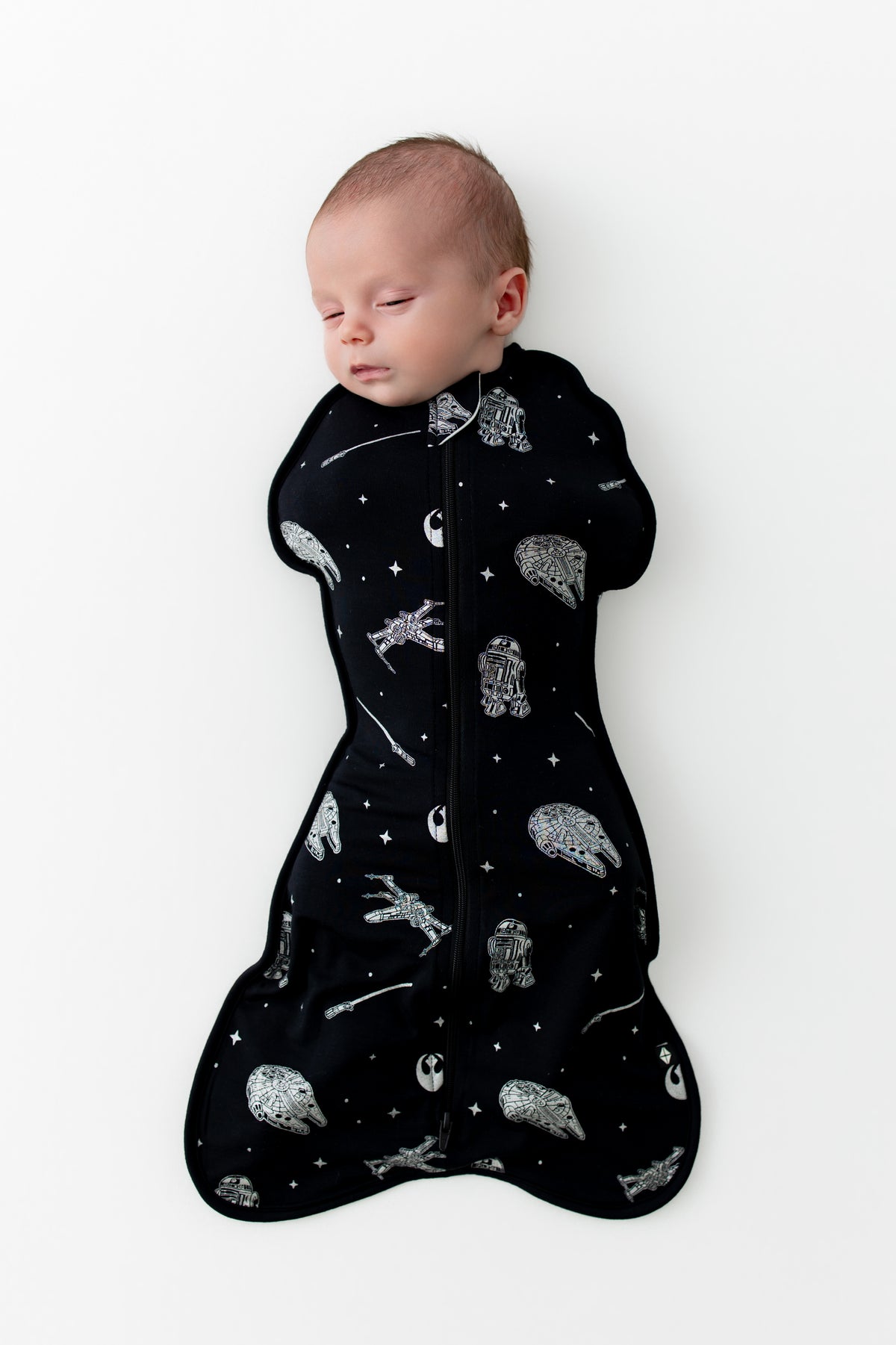 Sleeping newborn wearing the Swaddle Bag in STAR WARS™ 0.5 on a white surface