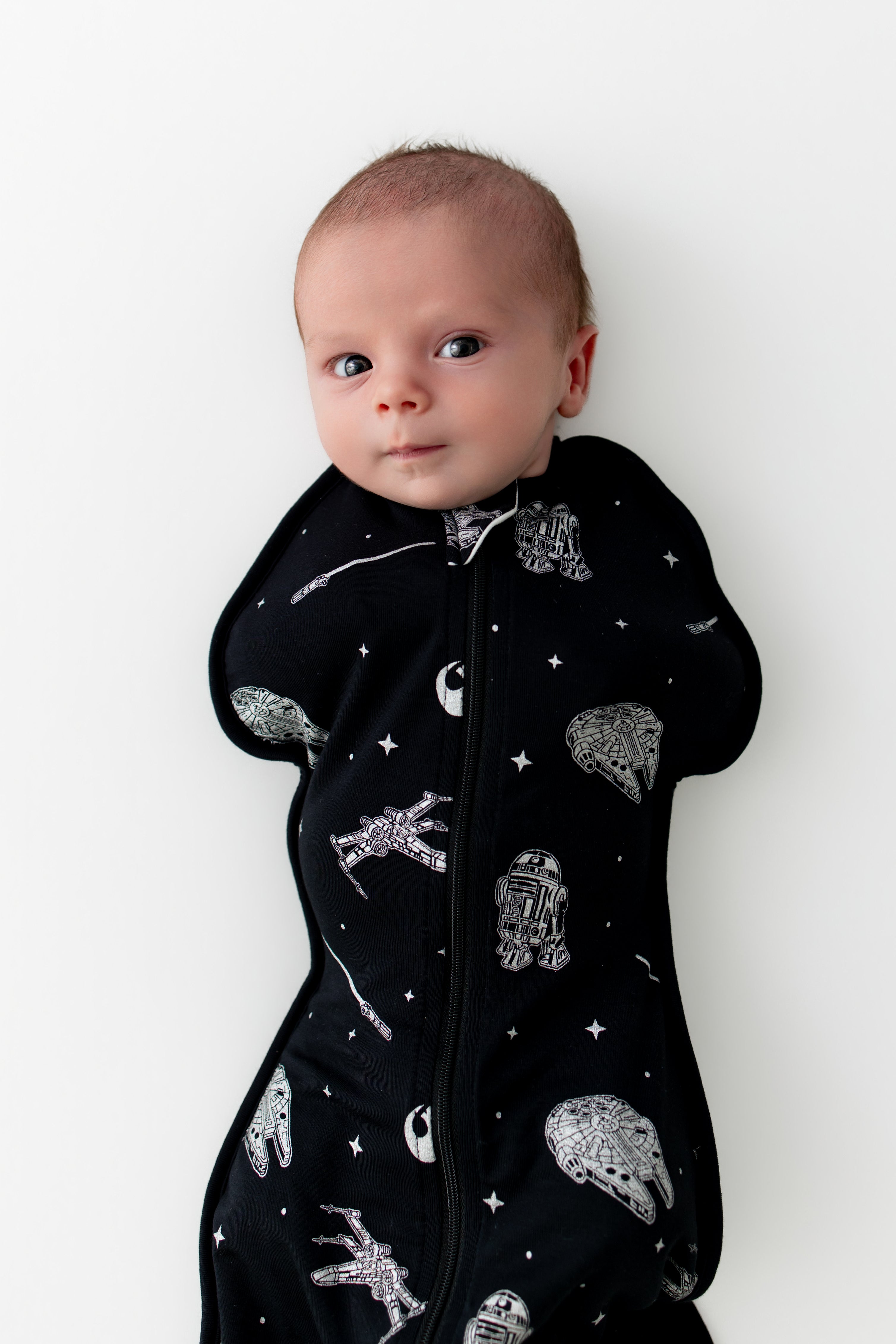 Newborn laying on a white surface wearing the Swaddle Bag in STAR WARS™ 0.5