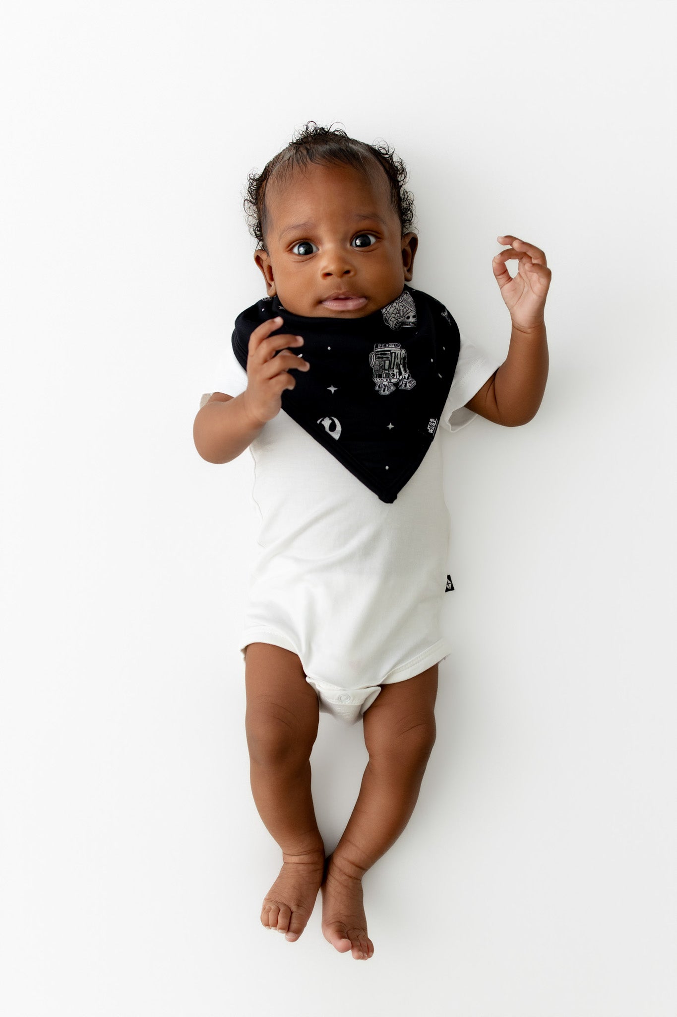 Infant laying on a white surface wearing the Bib in STAR WARS™ paired with a white short sleeve bodysuit