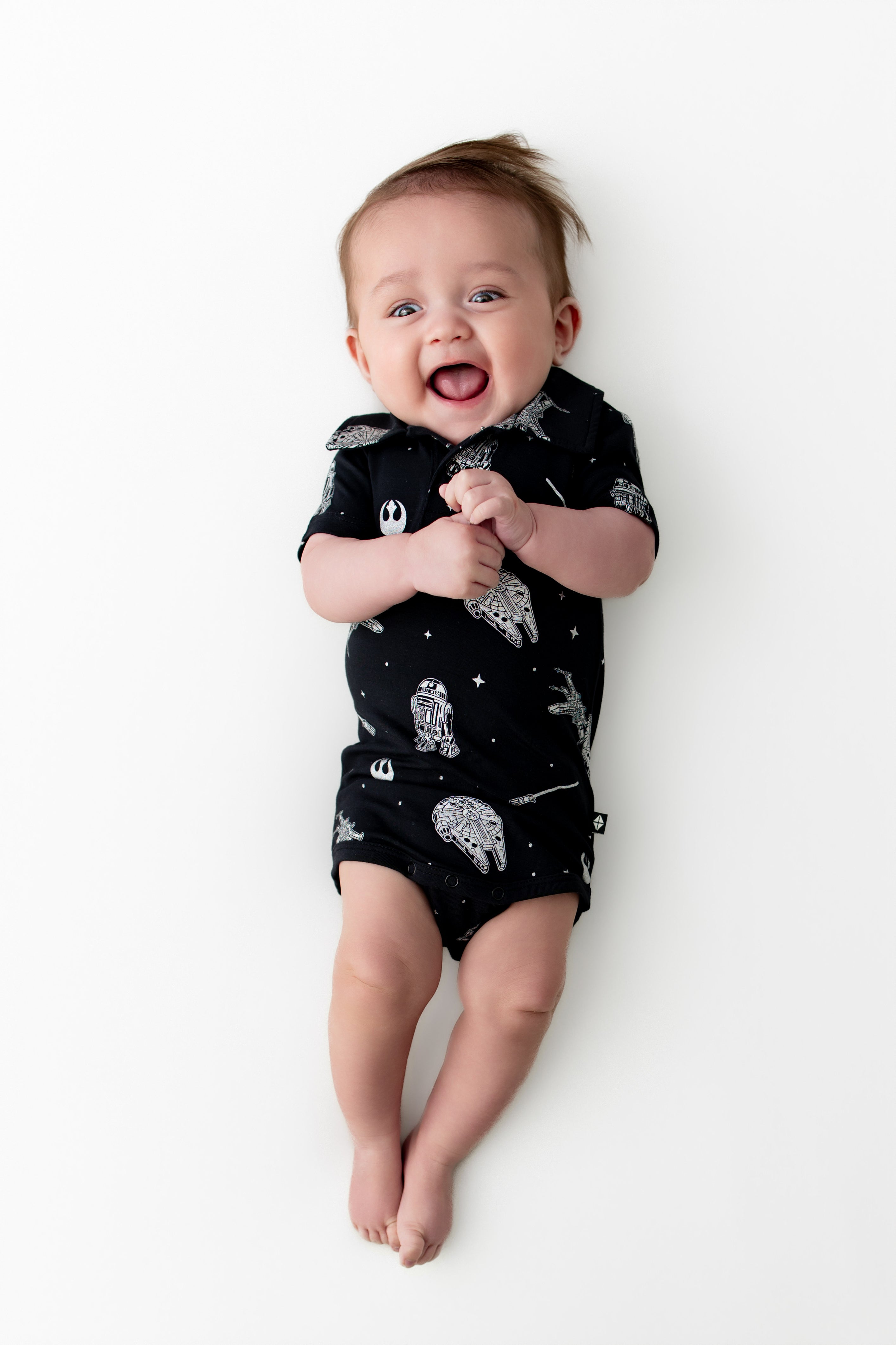 Smiling infant wearing the Polo Bodysuit in STAR WARS™ on a white surface