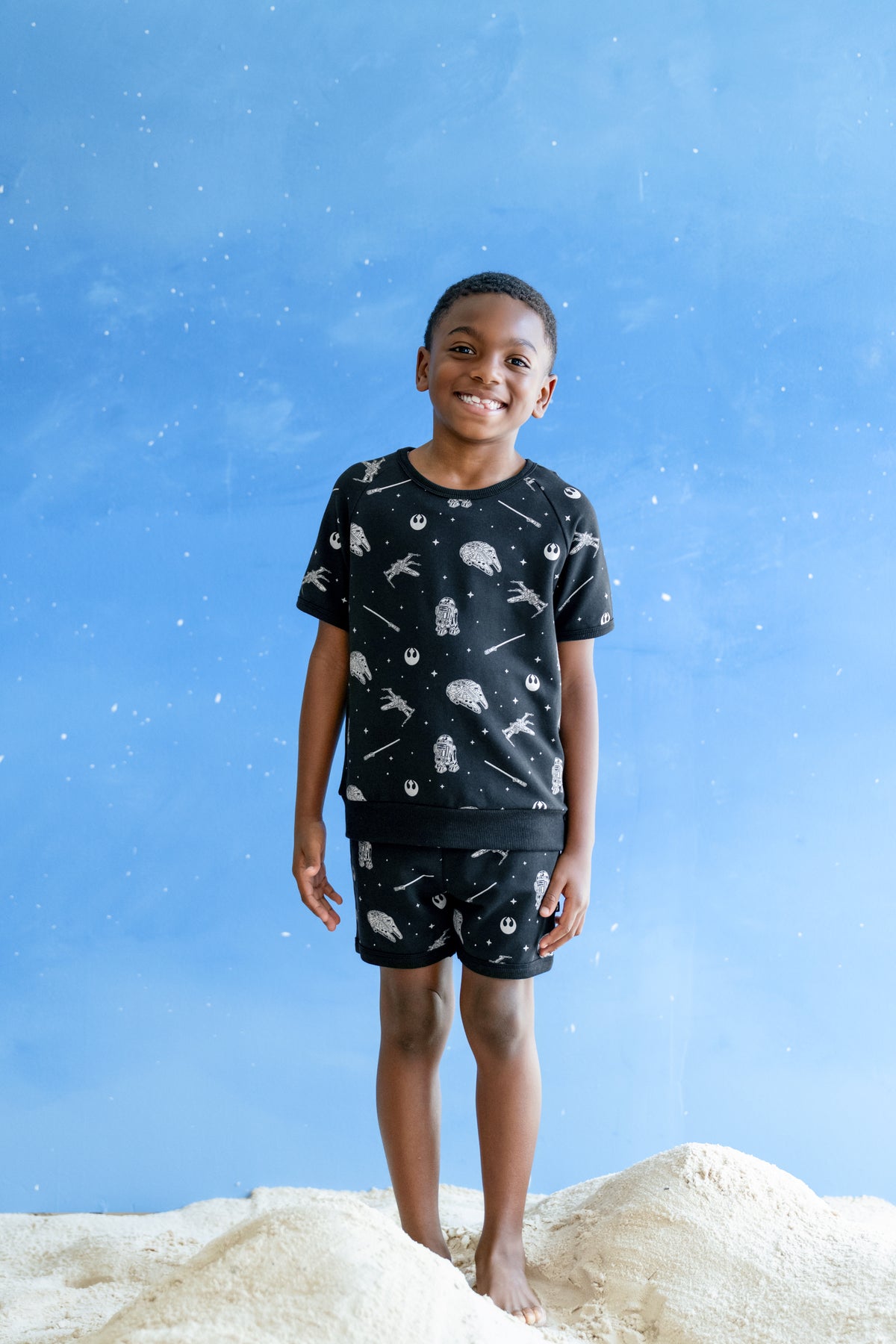 Young boy modeling the Short Sleeve Jogger Set in STAR WARS™ standing in sand and a blue sky backdrop