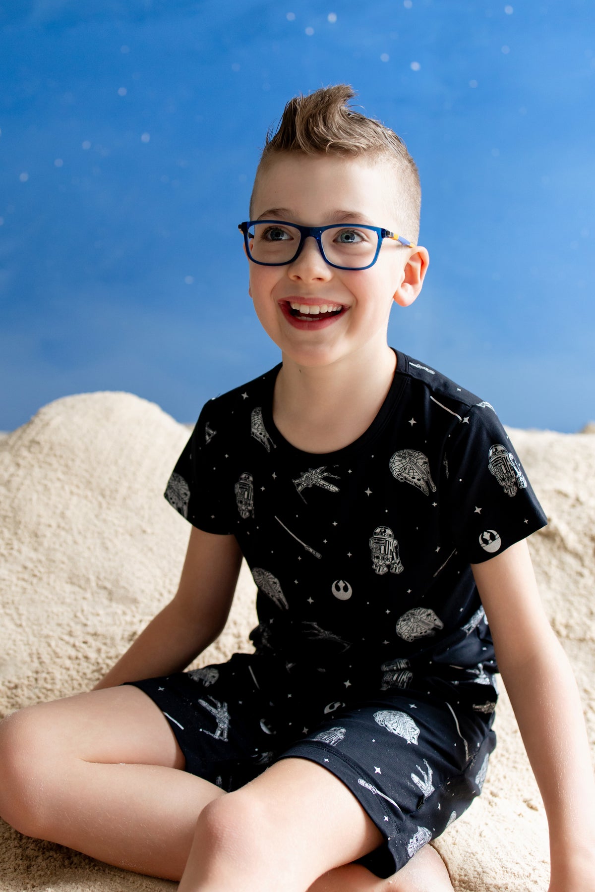 Young boy sitting in sand smiling wearing the Toddler Basic Tee in STAR WARS™