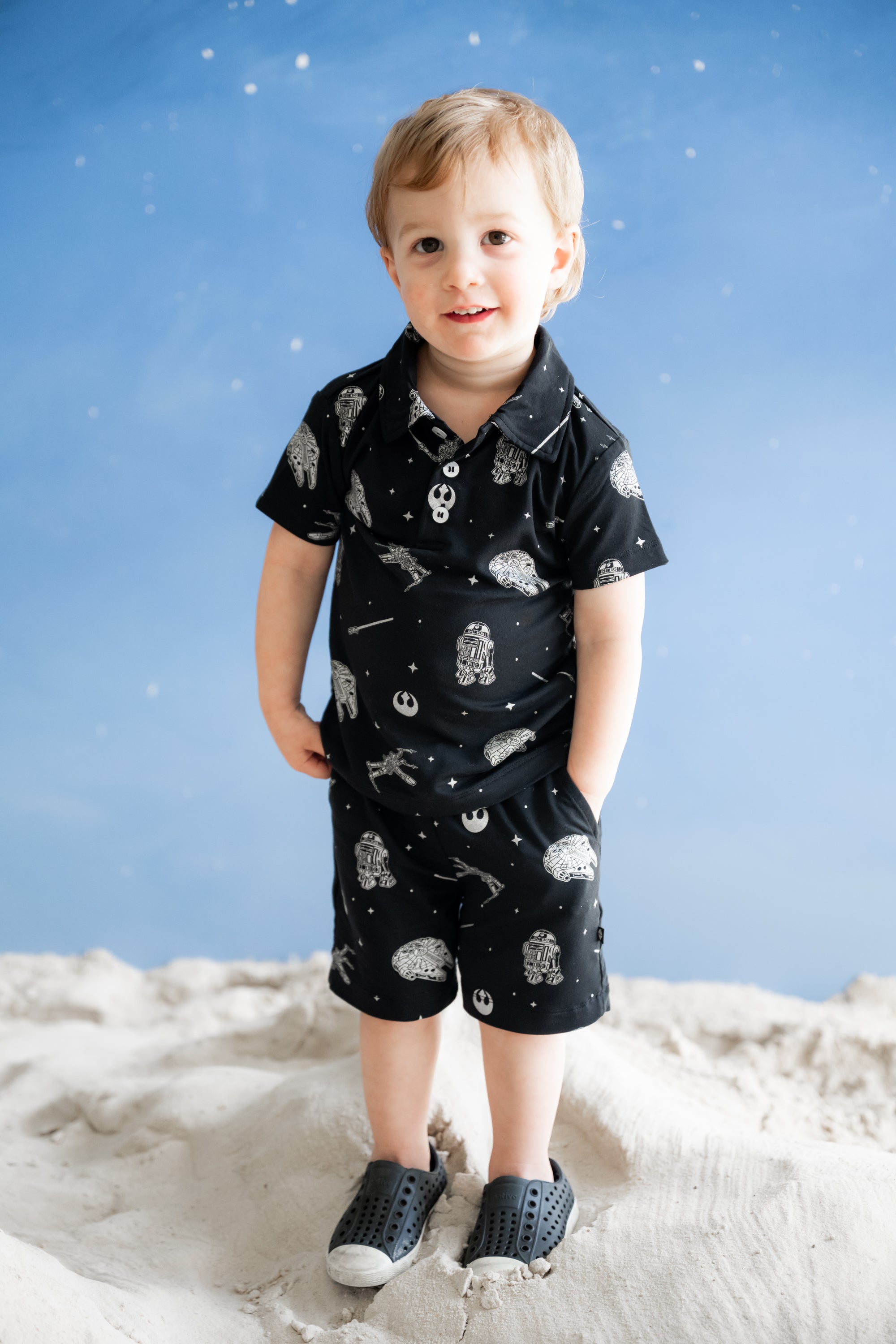 Young boy standing wearing the Toddler Short Sleeve Polo in STAR WARS™ with matching drawstring shorts