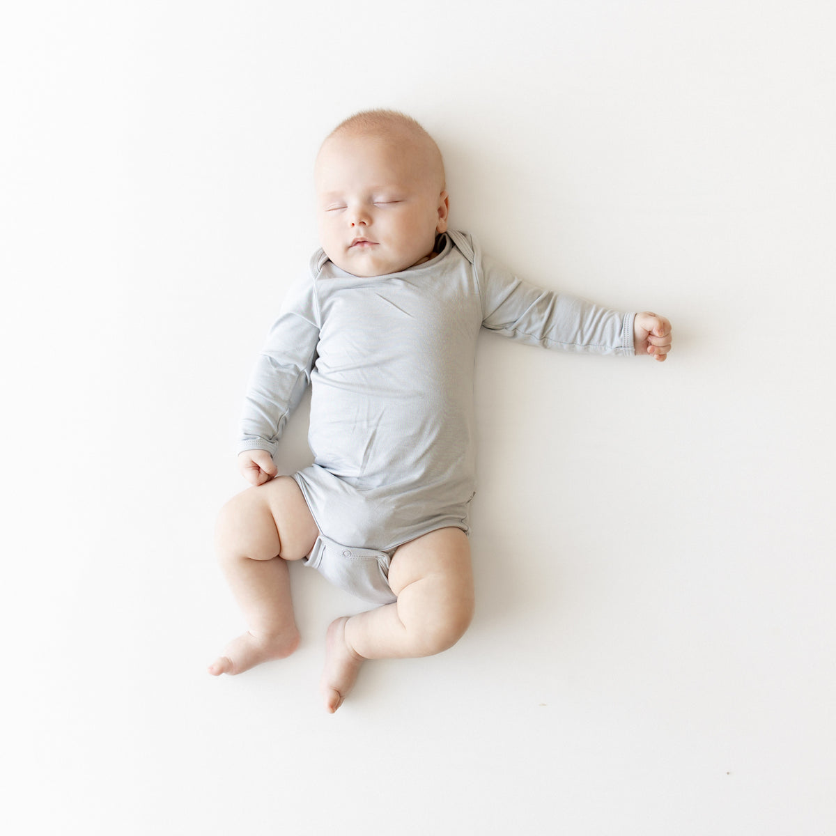 Baby in a gray onesie lying on a white surface