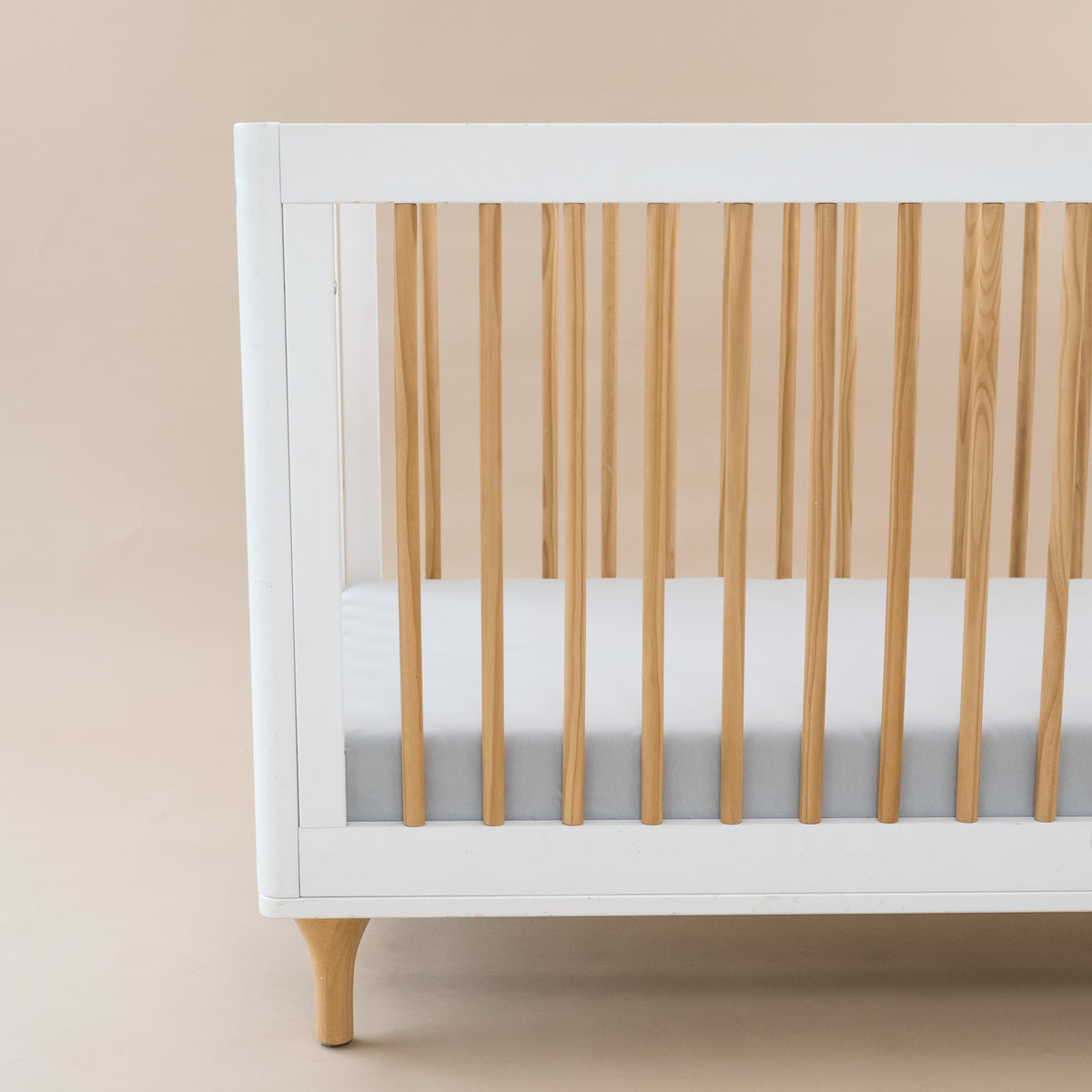 Crib Sheet in Storm shown on a mattress in a modern white and wooden crib