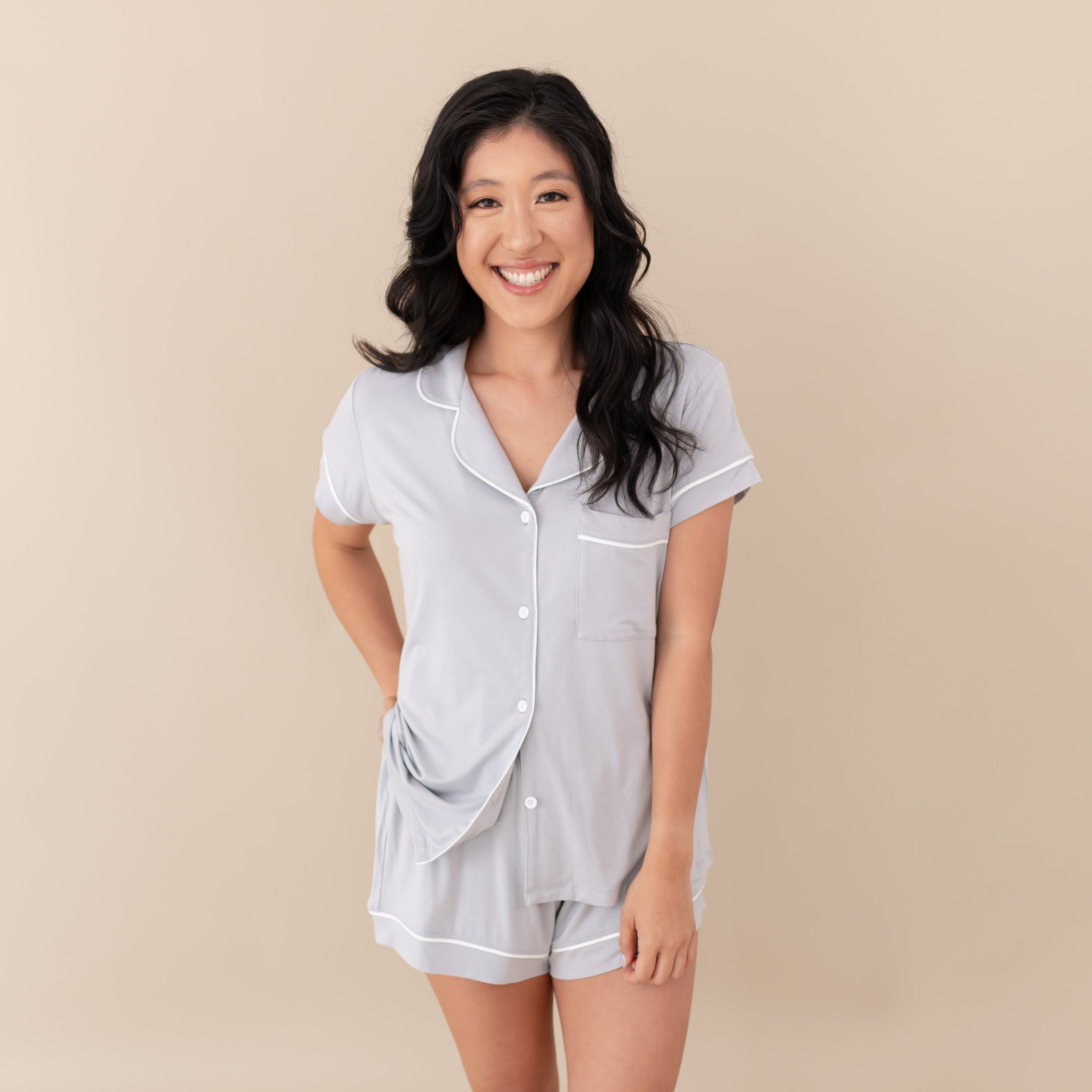 Woman modeling Women’s Short Sleeve Pajama Set in Storm with Cloud Trim with a tan backdrop.