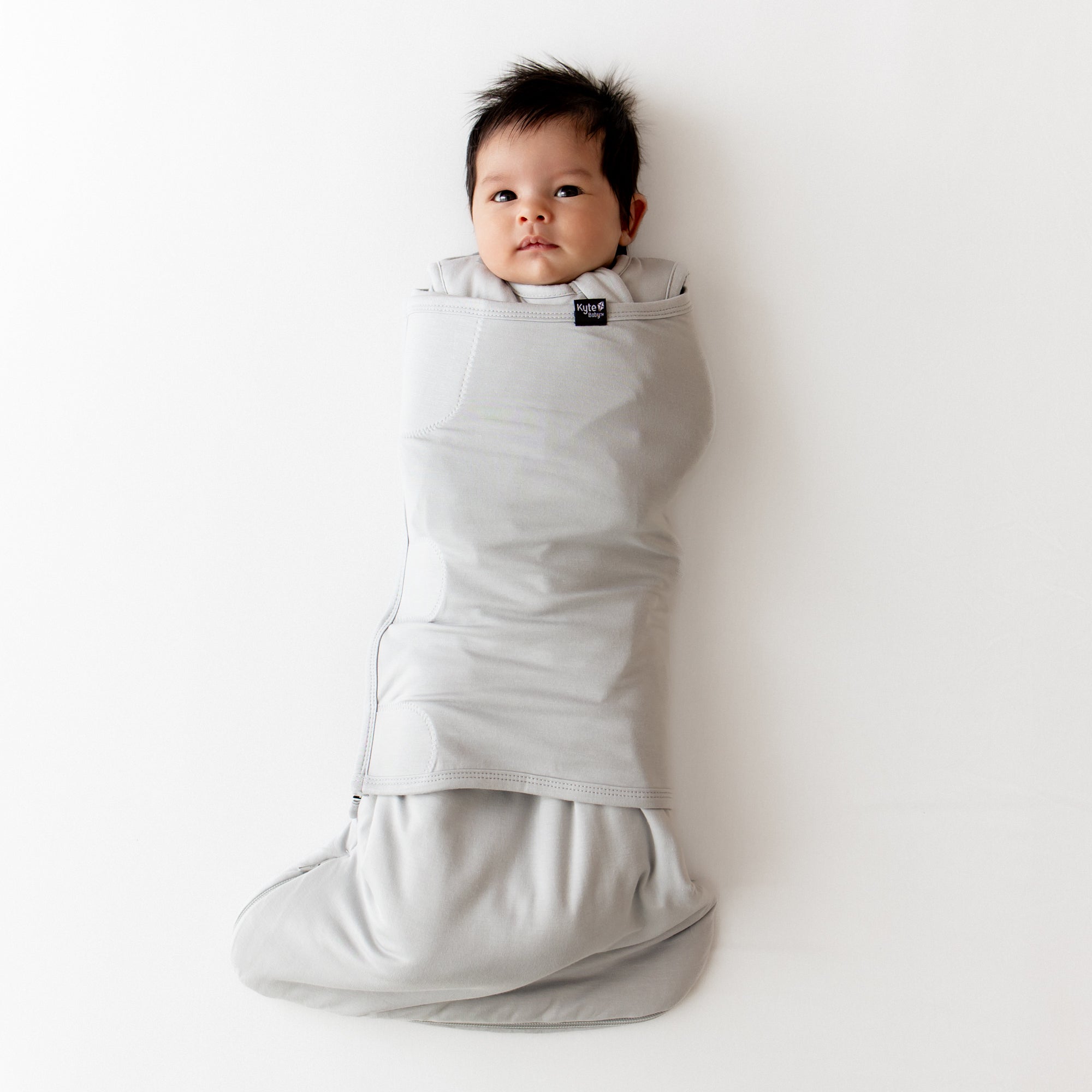 Baby wrapped in a gray swaddler on a white background