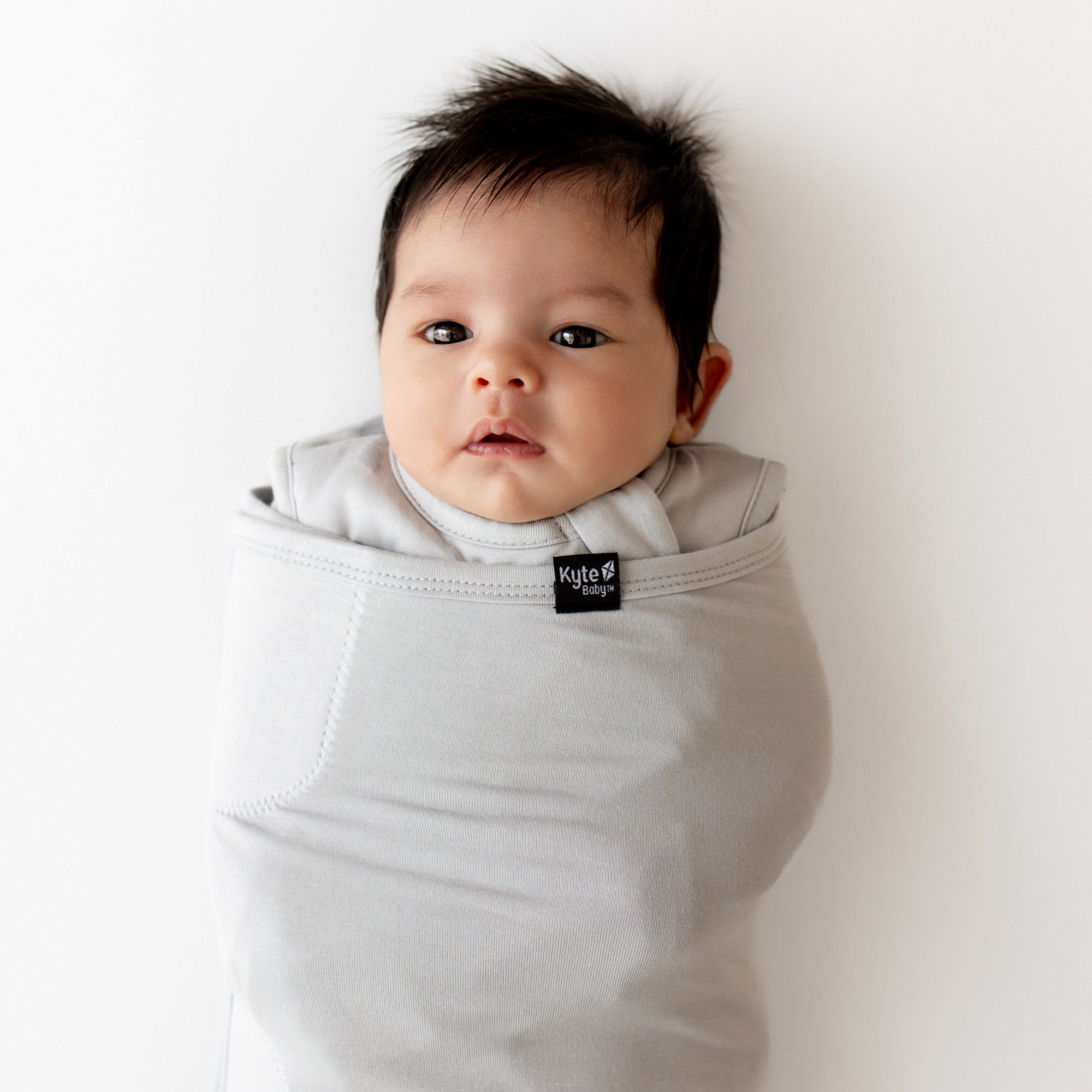 Baby wrapped in a Kyte Baby swaddler on a white background