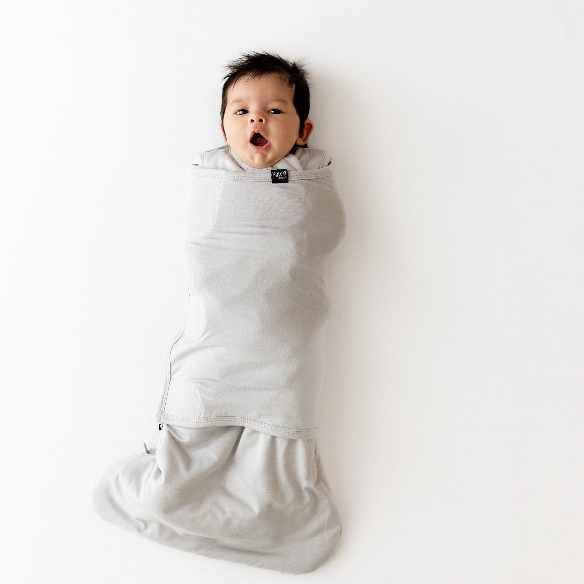 Baby yawning and wrapped in a gray swaddler on a white background