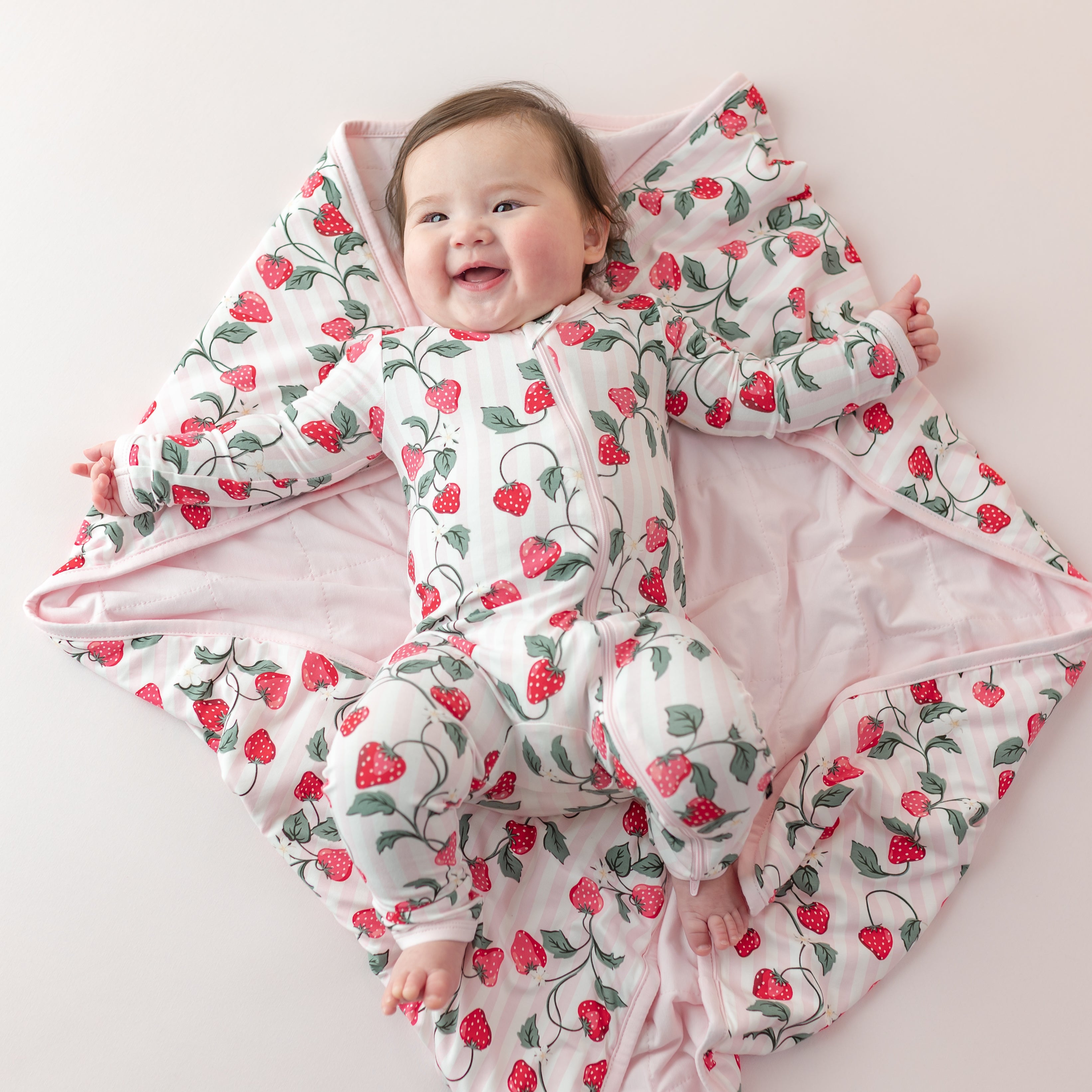 Smiling infant laying on the soft and luxurious Baby Blanket in Strawberry Fields 1.0 wearing the matching zippered romper