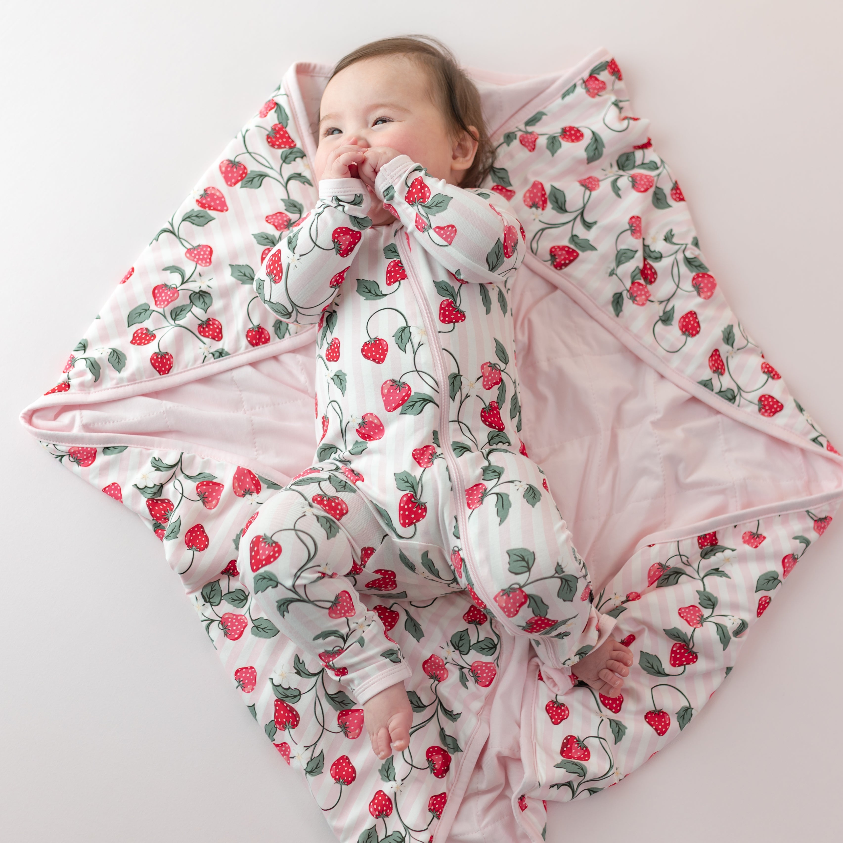 Smiling infant laying on a Baby Blanket in Strawberry Fields 1.0 wearing a matching zippered romper