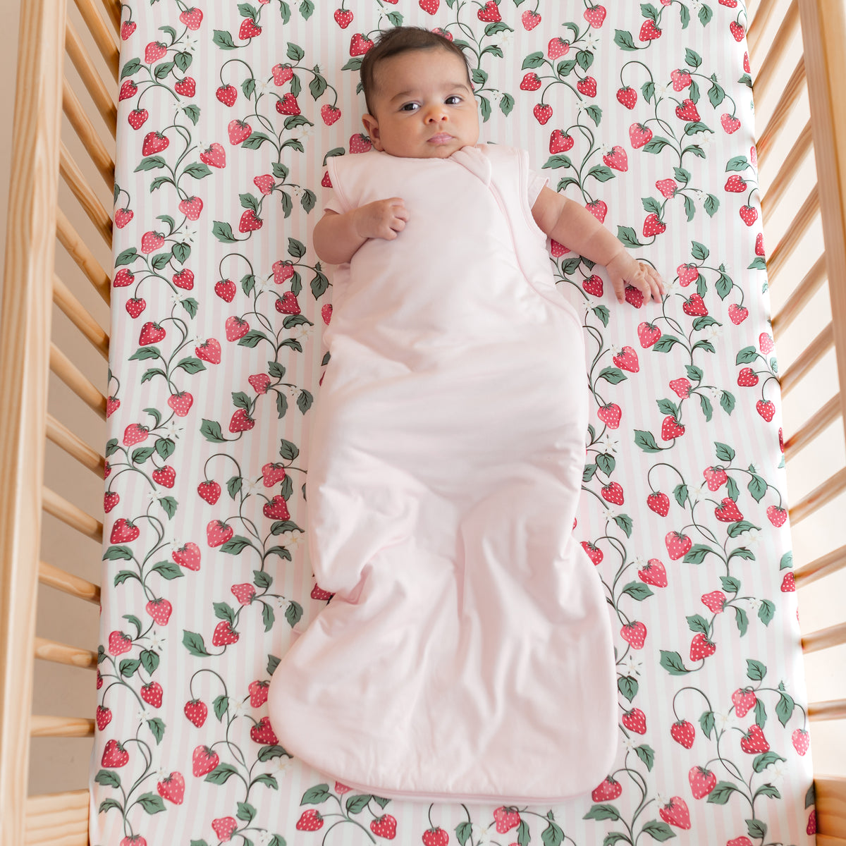 Infant laying in a crib on Crib Sheet in Strawberry Fields wearing a light pink sleep bag