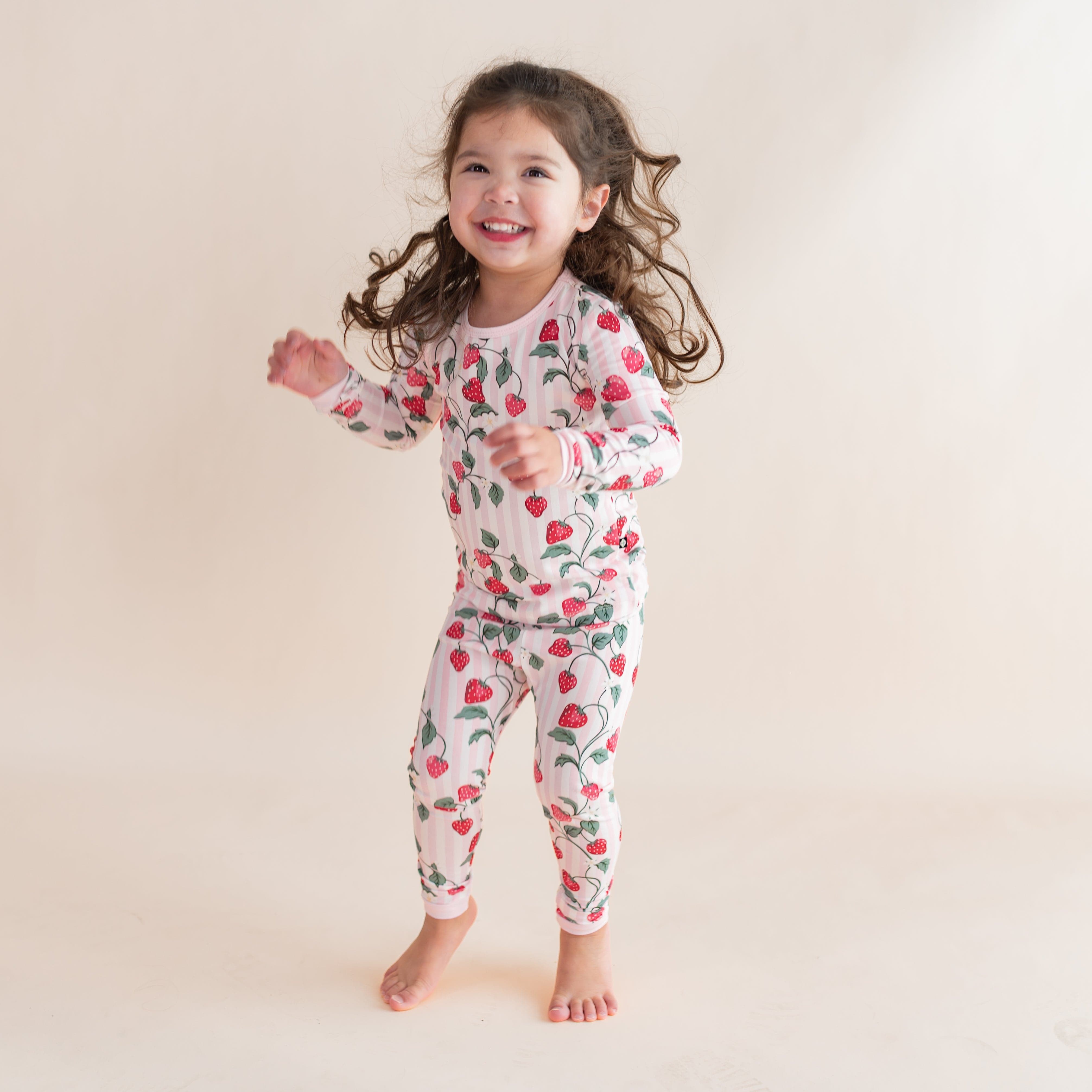 Young girl jumping wearing the Long Sleeve Pajamas in Strawberry Fields in front of a light neutral background