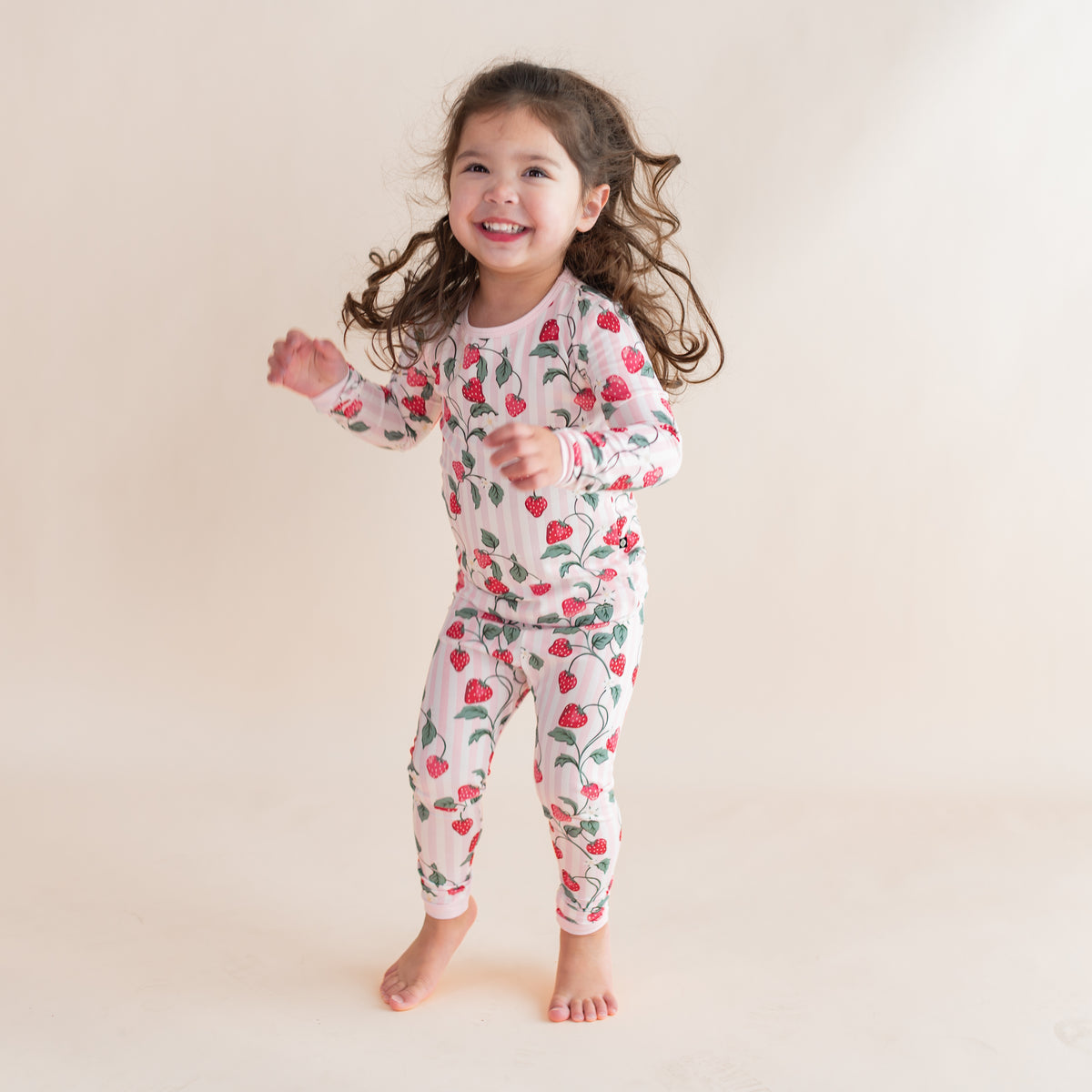Young girl jumping wearing the Long Sleeve Pajamas in Strawberry Fields in front of a light neutral background