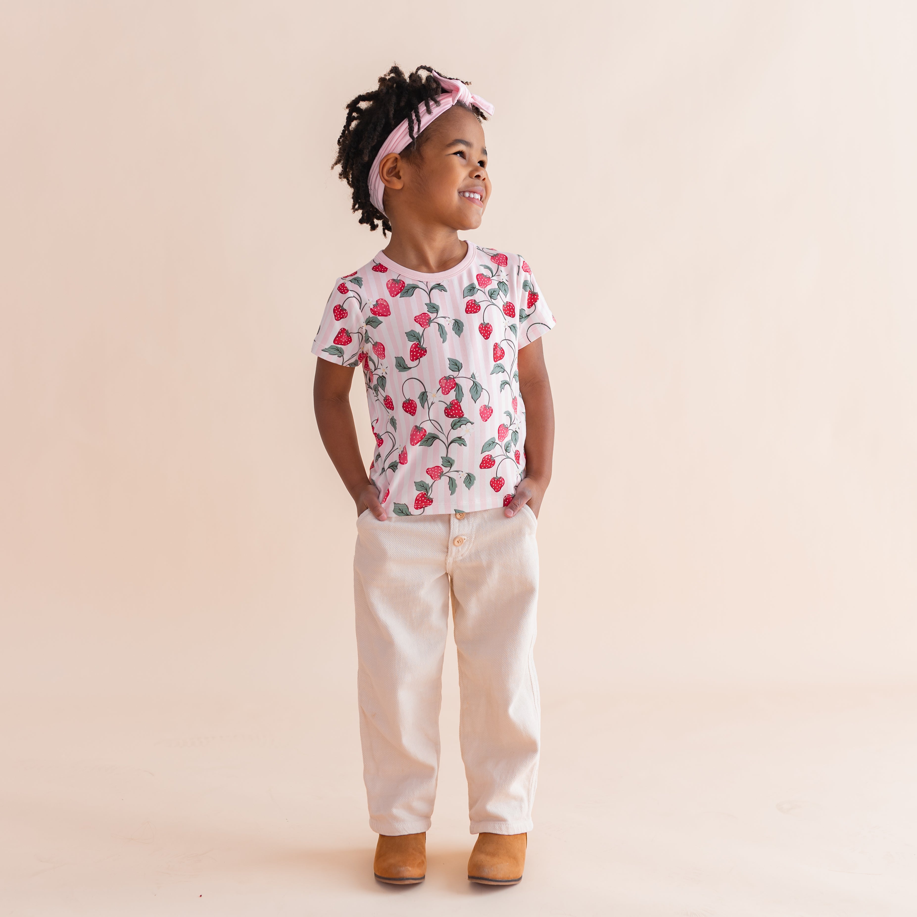 Young girl standing in front of a light beige background wearing the Toddler Basic Tee in Strawberry Fields with light neutral pants