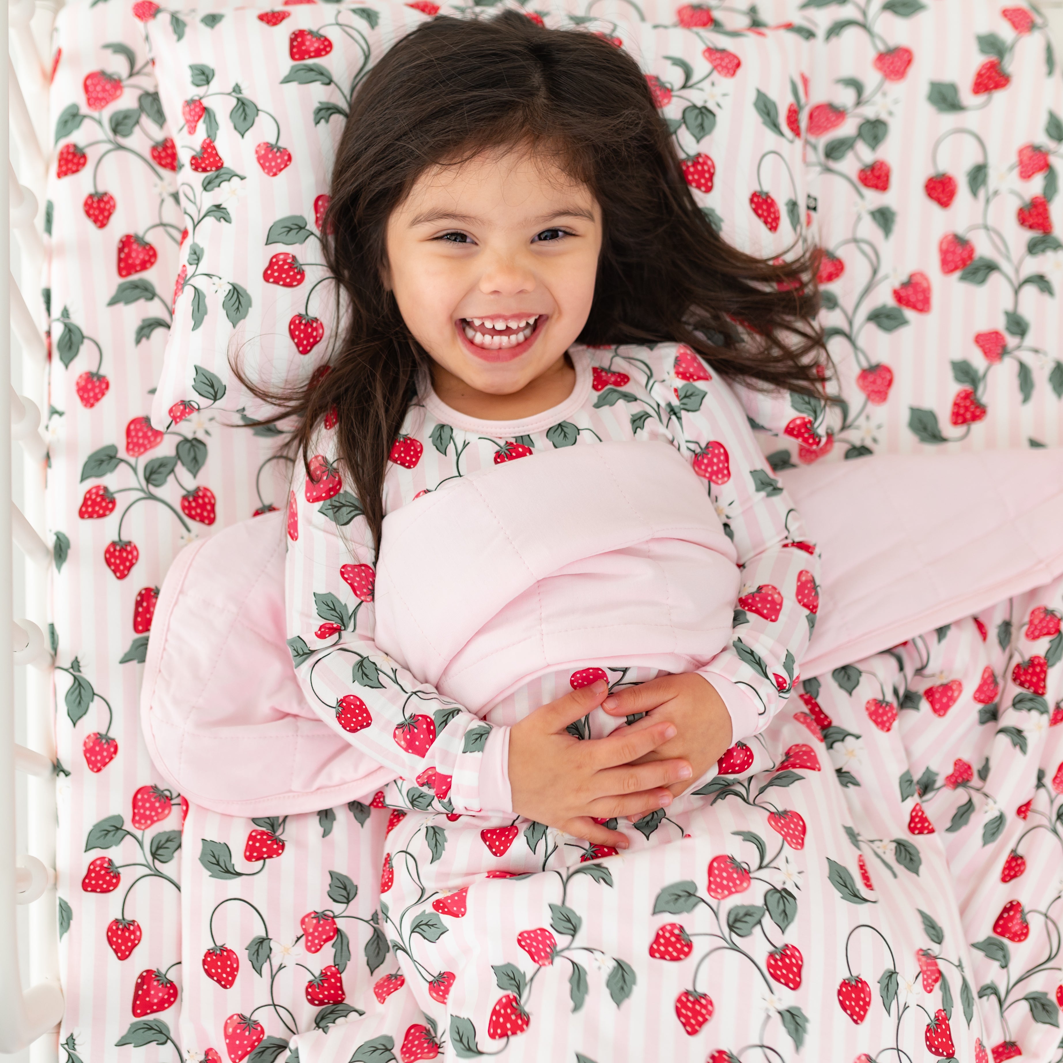 Young girl laying in bed with the Toddler Blanket in Strawberry Fields 1.0 overtop of her