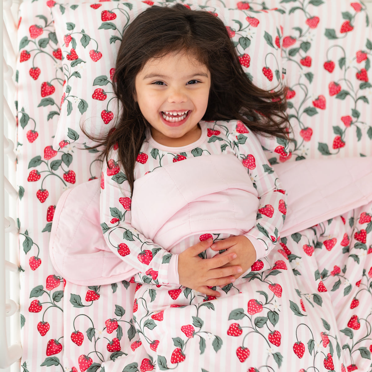 Young girl laying in bed with the Toddler Blanket in Strawberry Fields 1.0 overtop of her